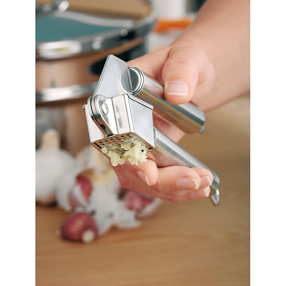 Eine Hand benutzt einen silbernen Knoblauchpresse, um Knoblauch zu zerdrücken.