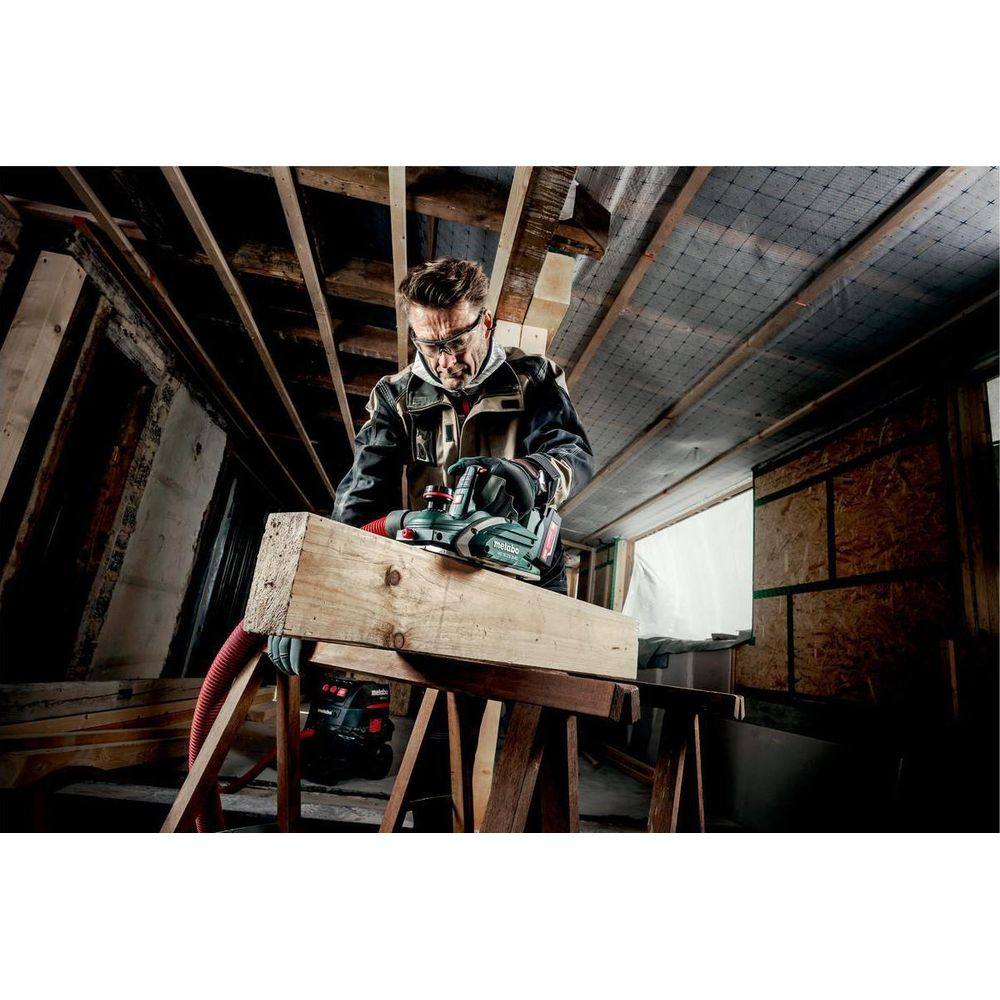 Mann hobelt Holz mit Elektrowerkzeug in einer Baustelle.