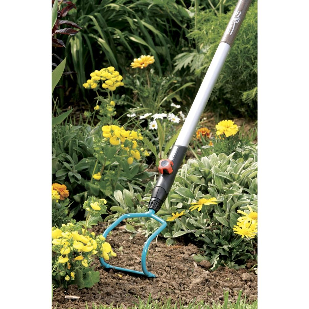 Ein Gartenwerkzeug mit blauem Kopf im Beet mit gelben Blumen.