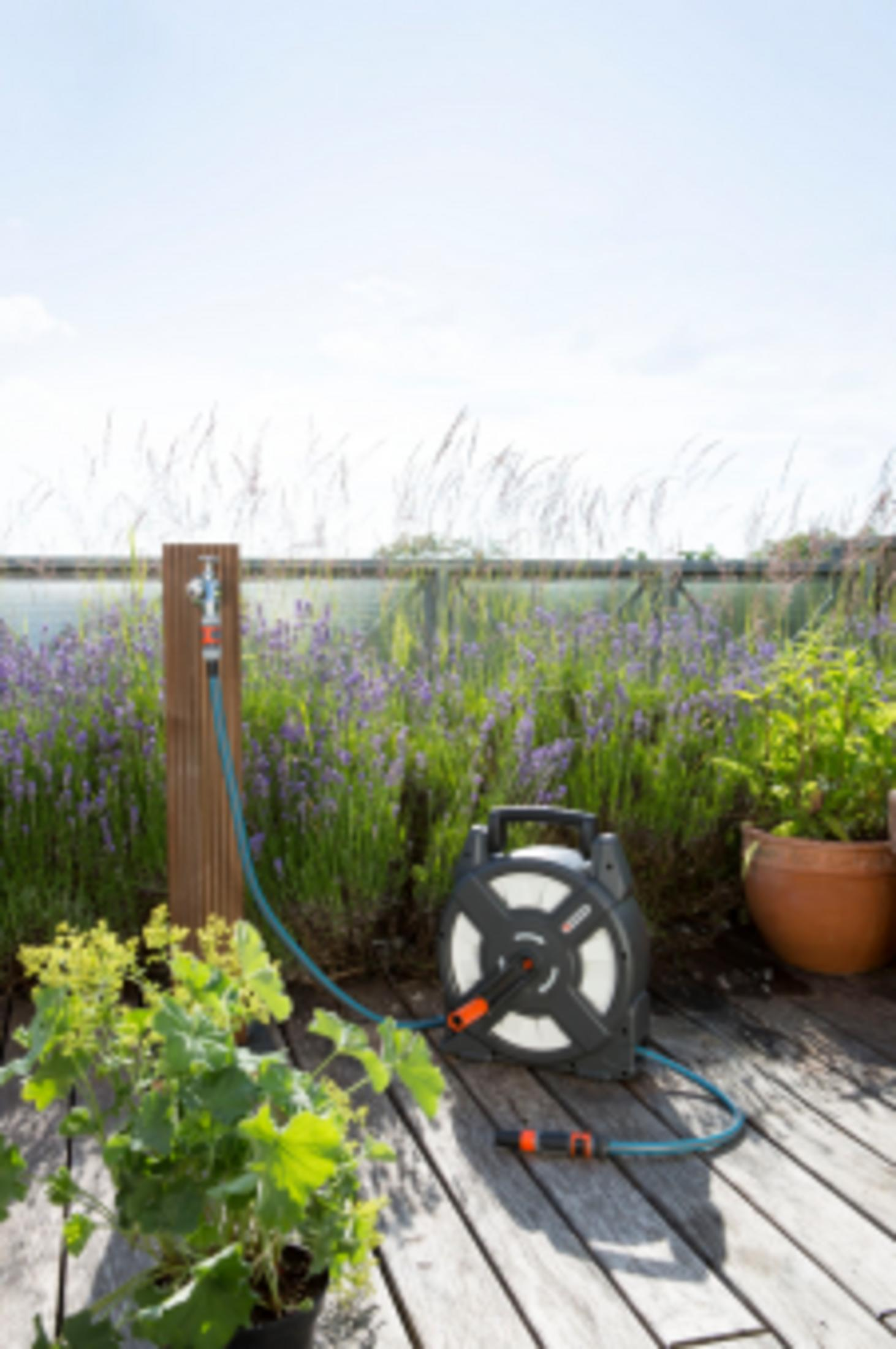 Gartenschlauchaufroller auf Holzdeck mit Lavendel und Topfpflanzen.