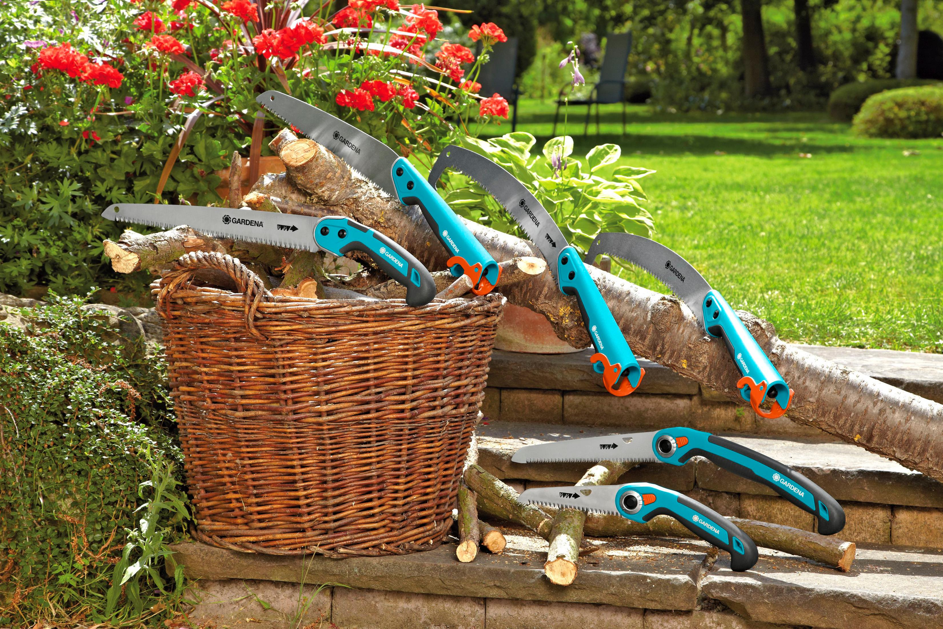 Piły ogrodowe leżą na polanach obok wiklinowego kosza w ogrodzie.