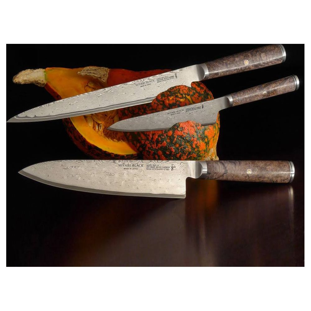 Trzy ostrza noży damasceńskich z brązowymi rękojeściami spoczywają na dyni.