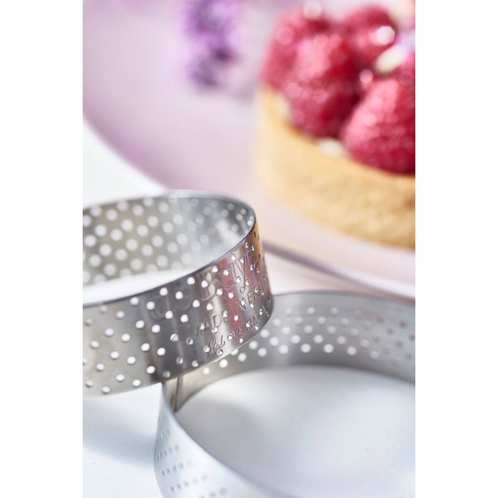 Deux anneaux métalliques ronds à motifs perforés reposent devant une tartelette aux fraises.