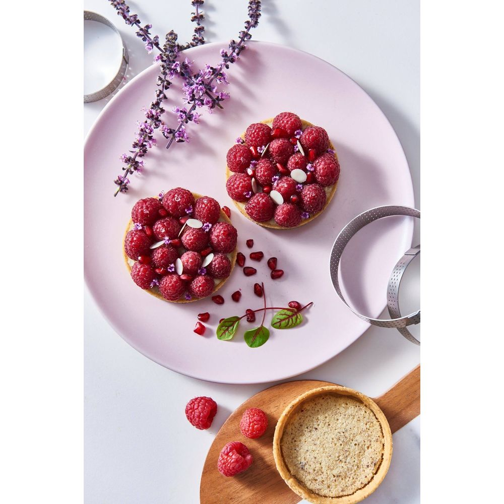 Deux tartes aux framboises avec des graines de grenade et des amandes sur une assiette rose.