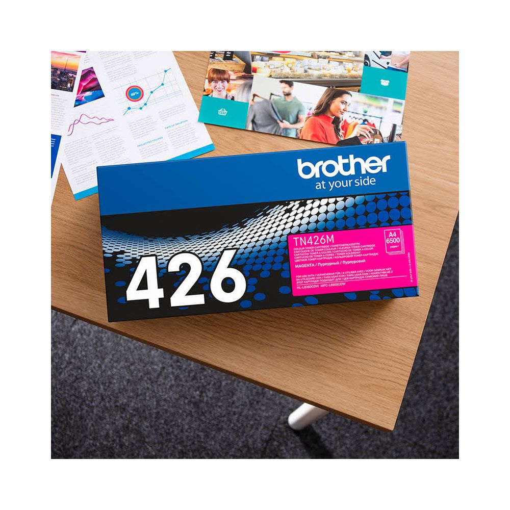 Pudełko tonera Brother TN426M Magenta na drewnianym stole, z broszurami.