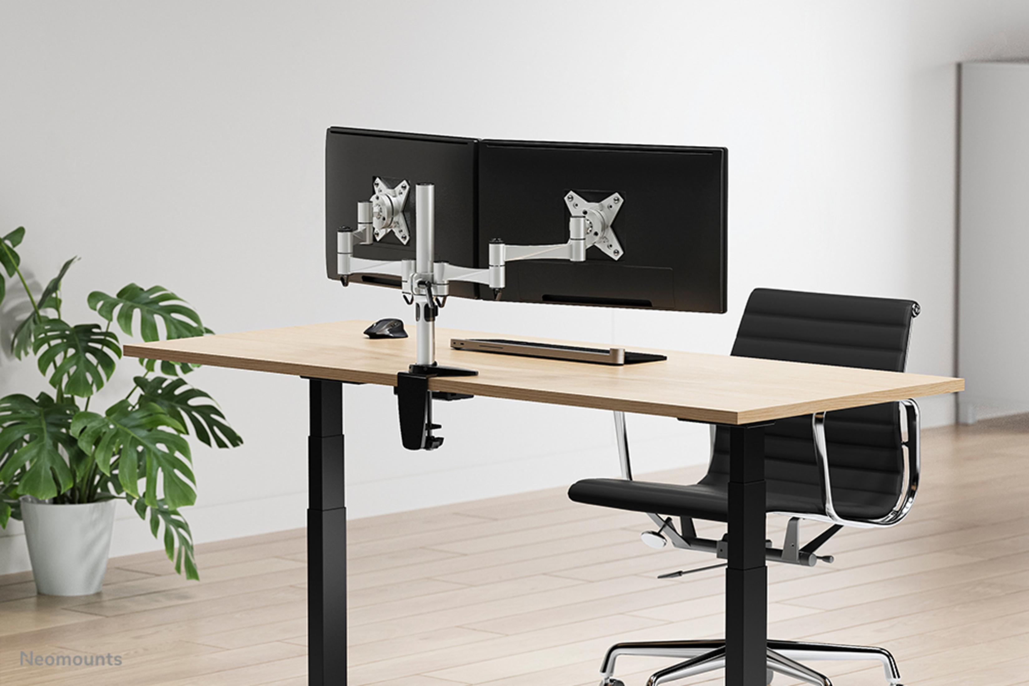Een bureau met twee monitoren, een zwarte stoel en een potplant.