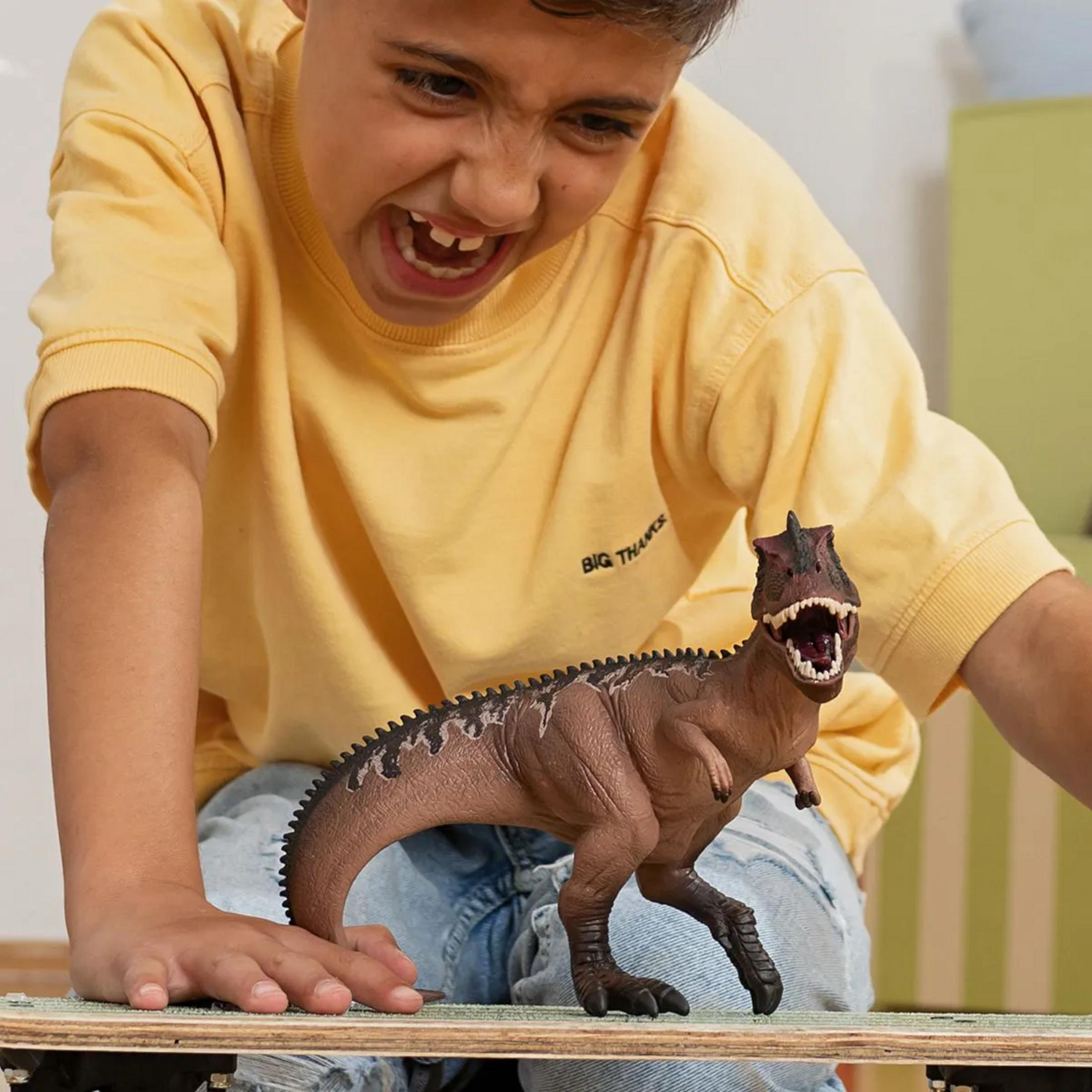 Un ragazzo con maglia gialla gioca con un dinosauro giocattolo.