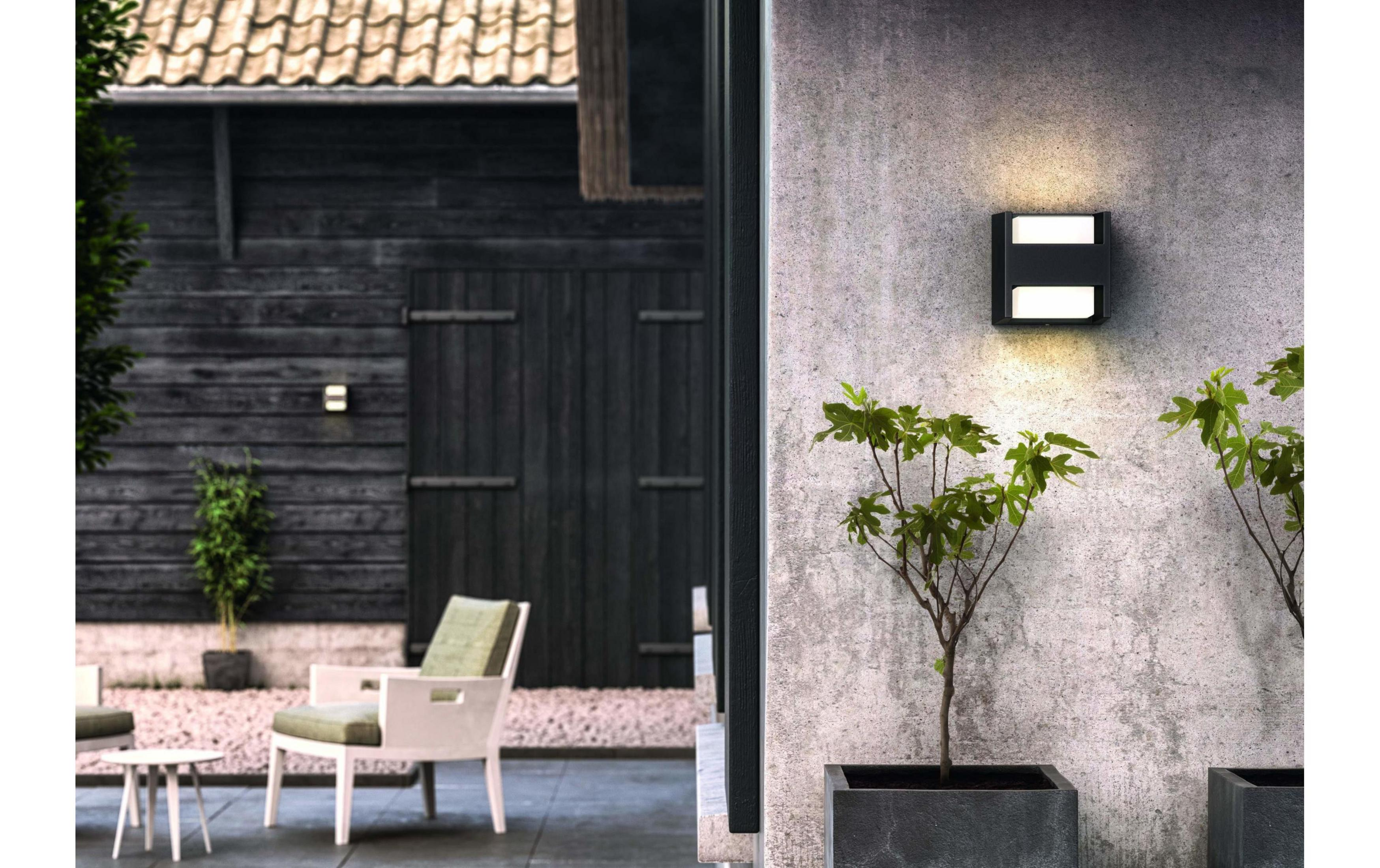 Aplique de pared exterior en pared de hormigón junto a plantas y cobertizo.