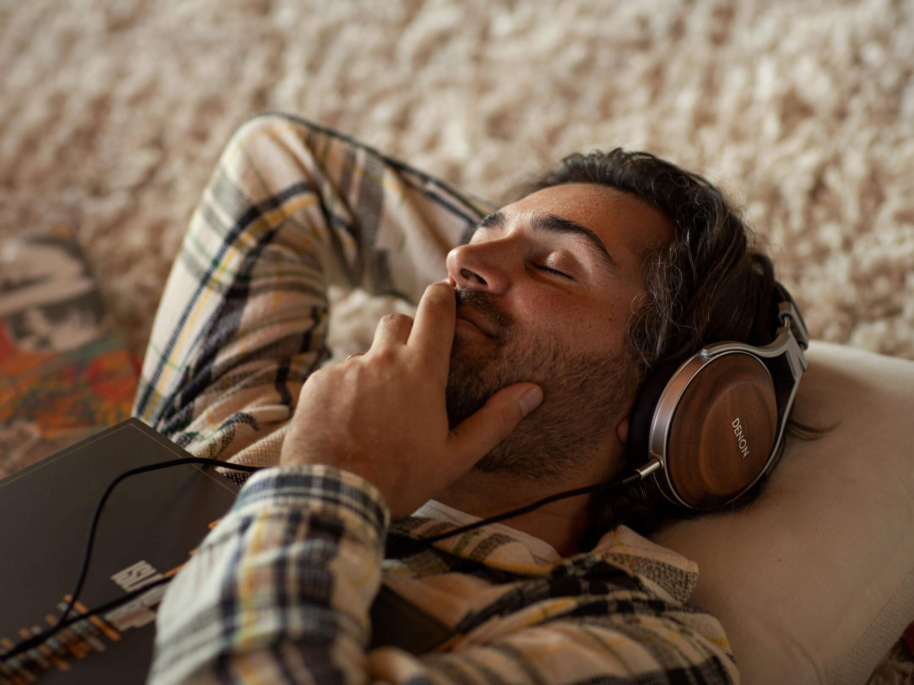 Mężczyzna w słuchawkach leży na dywanie, ręka na brodzie.