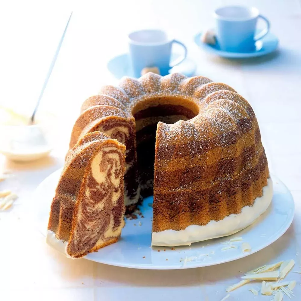 Marmorierter Gugelhupf mit Puderzucker und weißer Glasur, auf einem Teller.