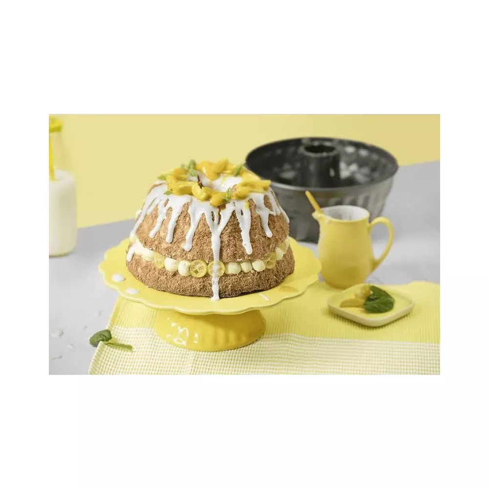 Ein Kuchen mit weißem Zuckerguss und Zitrone auf einem gelben Tortenständer.