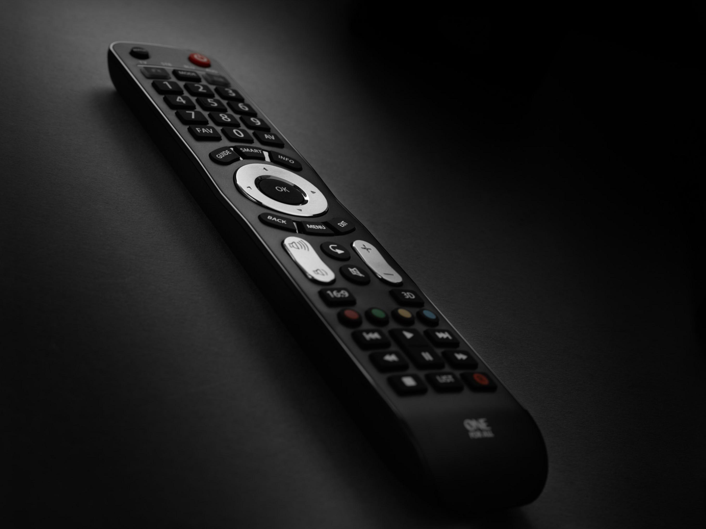 Black remote control with buttons, lying on a dark background.