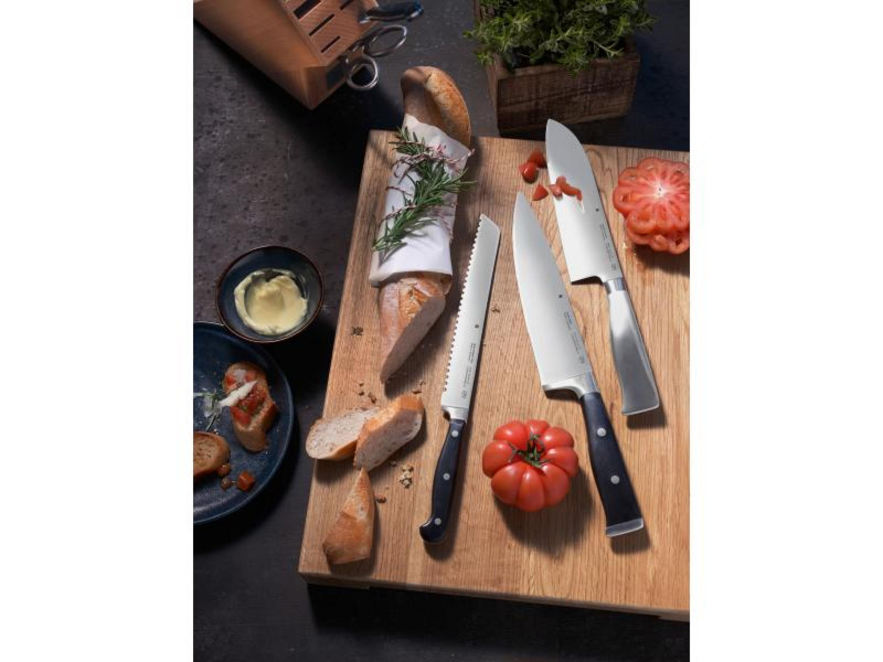 Küchenmesser, Brot, Tomaten und Butter auf einem Holzbrett.