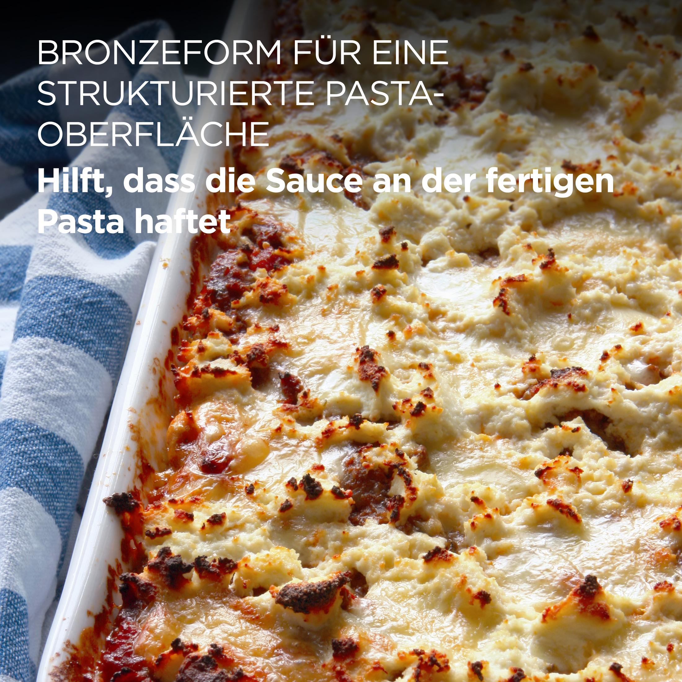 Piatto di pasta al forno gratinato con formaggio, accanto a un canovaccio a righe blu e bianche.
