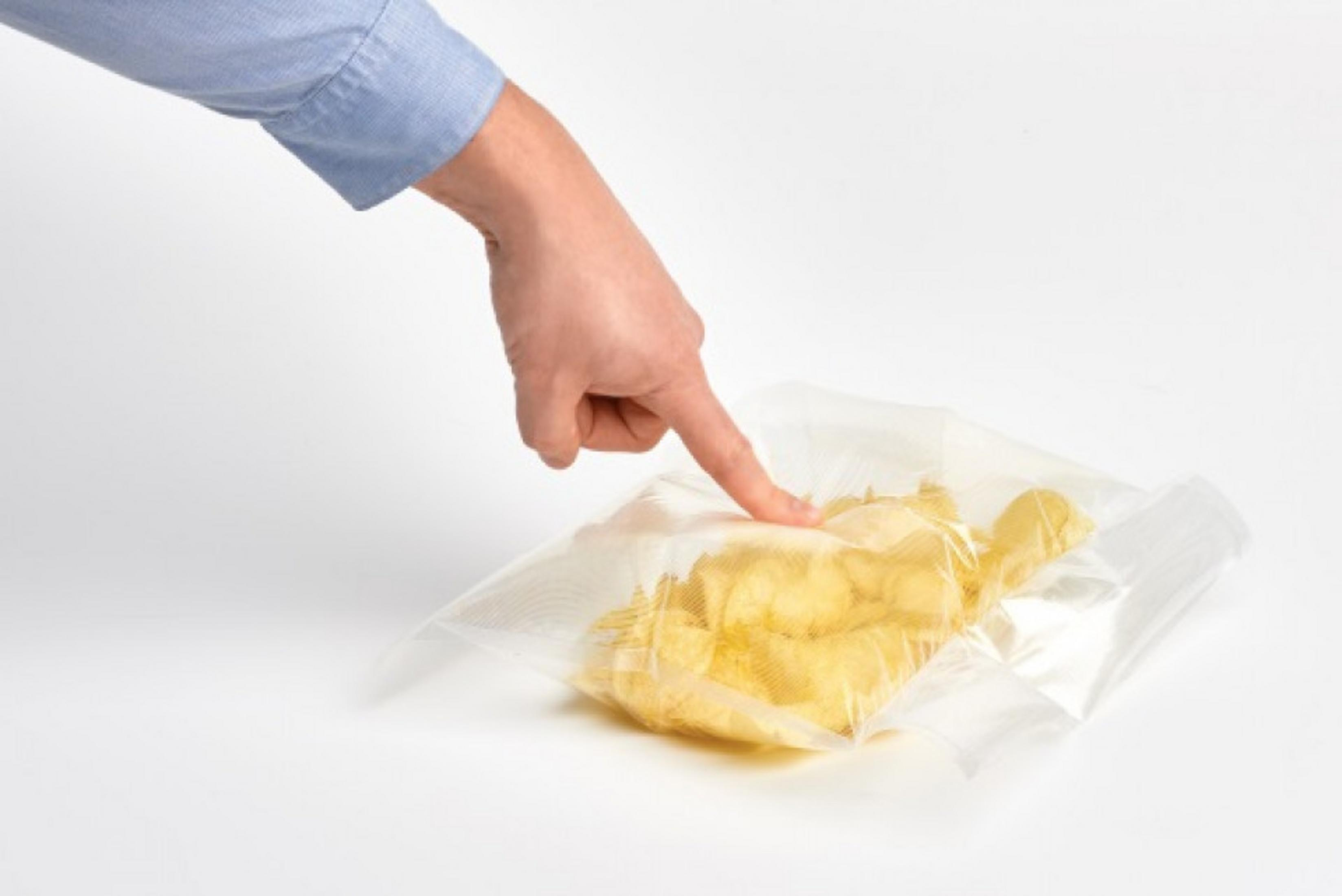 Eine Hand mit blauem Hemd drückt auf eine Plastiktüte mit Chips.