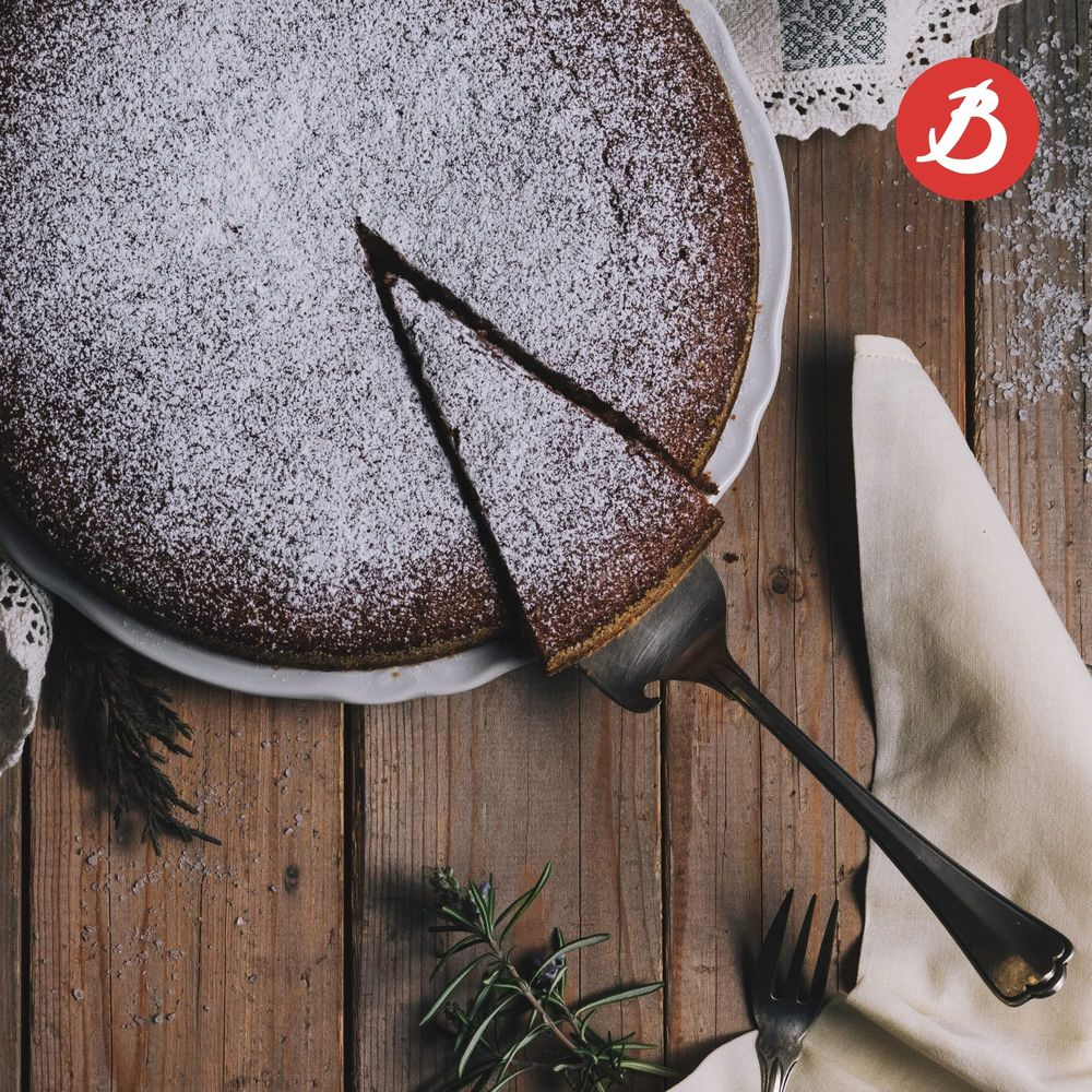 Ein runder Kuchen mit Puderzucker bestäubt, ein Stück wird herausgenommen.