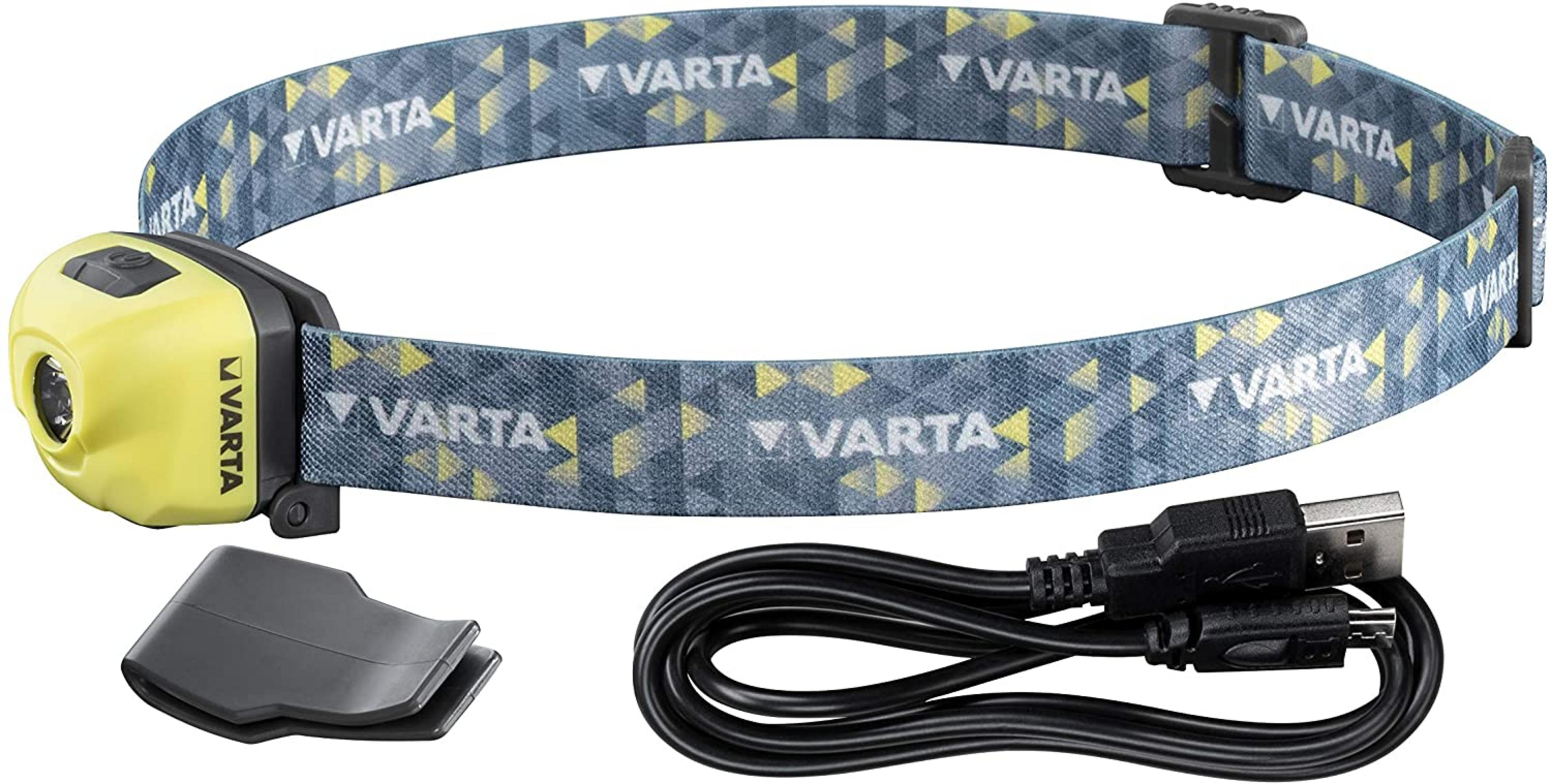 Une lampe frontale Varta jaune avec bandeau bleu, câble de chargement et support.