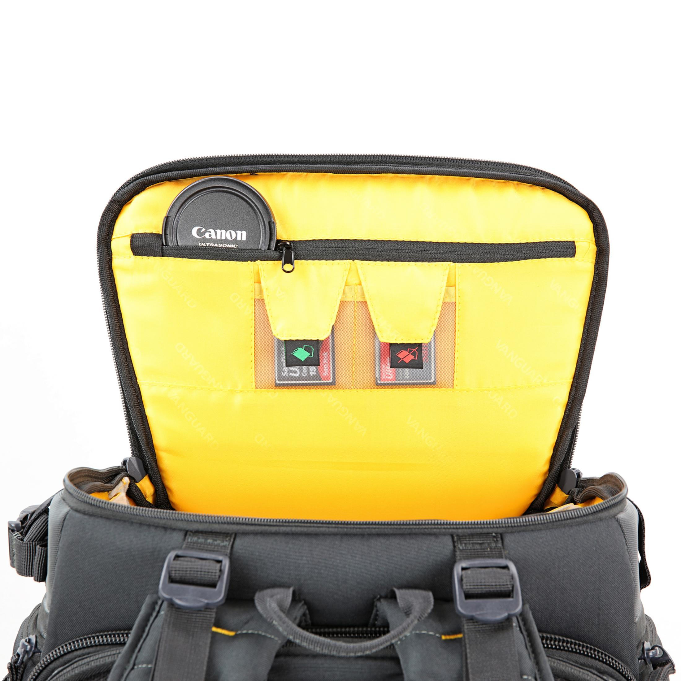 Ein offener grauer Rucksack mit gelbem Innenfutter. Ein Objektivdeckel liegt oben.