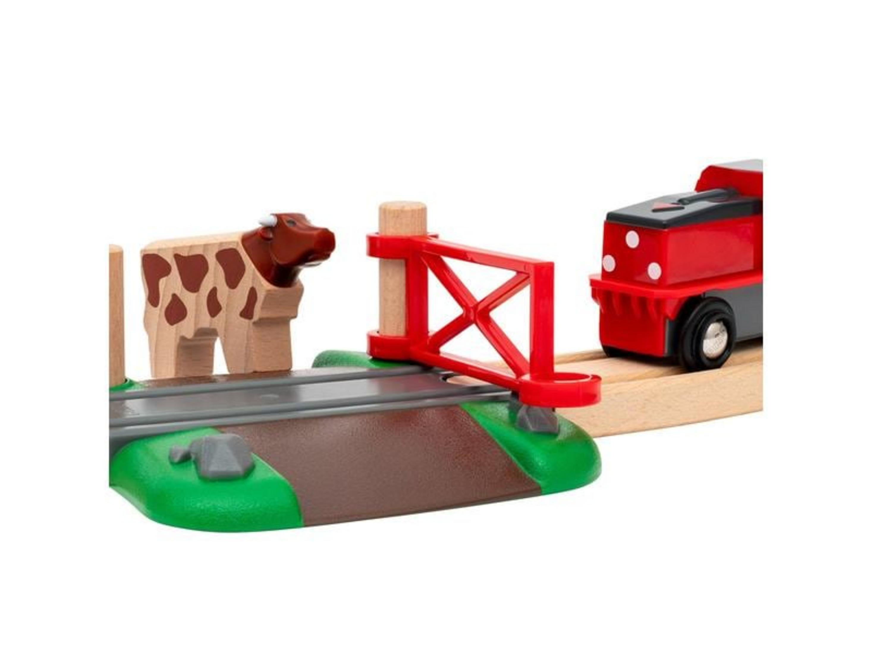 Drewniana lokomotywa zabawkowa przy czerwonej bramce, obok krowa.