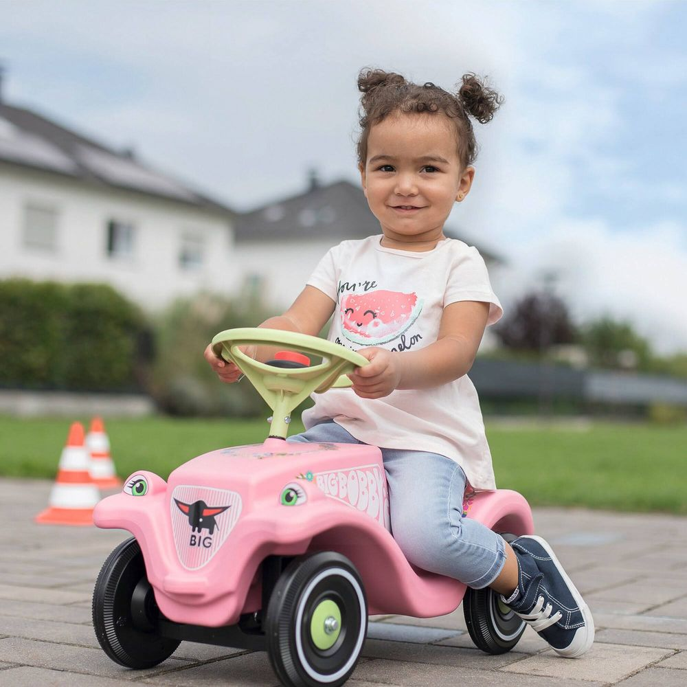 Ein kleines Mädchen fährt ein rosafarbenes Spielzeugauto mit einem Wassermelonen-T-Shirt.