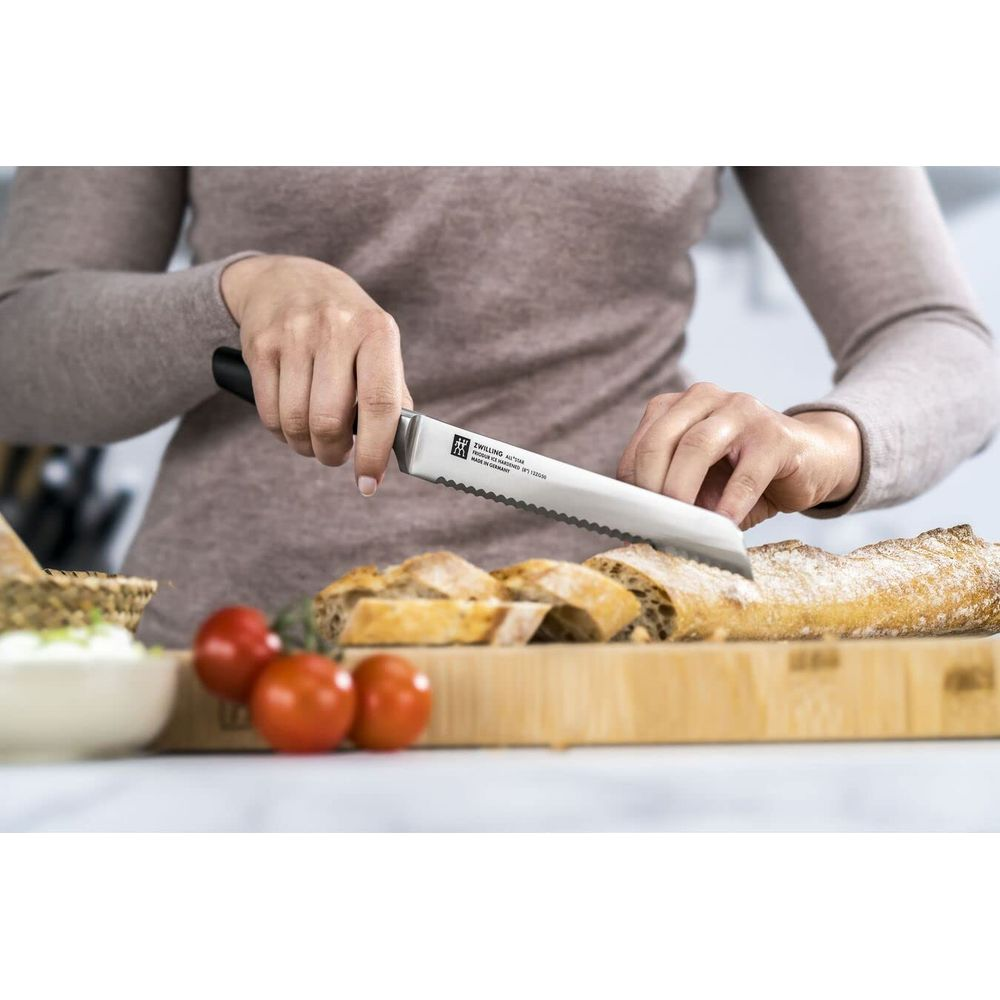 Eine Person schneidet ein Baguette auf einem Holzbrett mit einem Brotmesser.