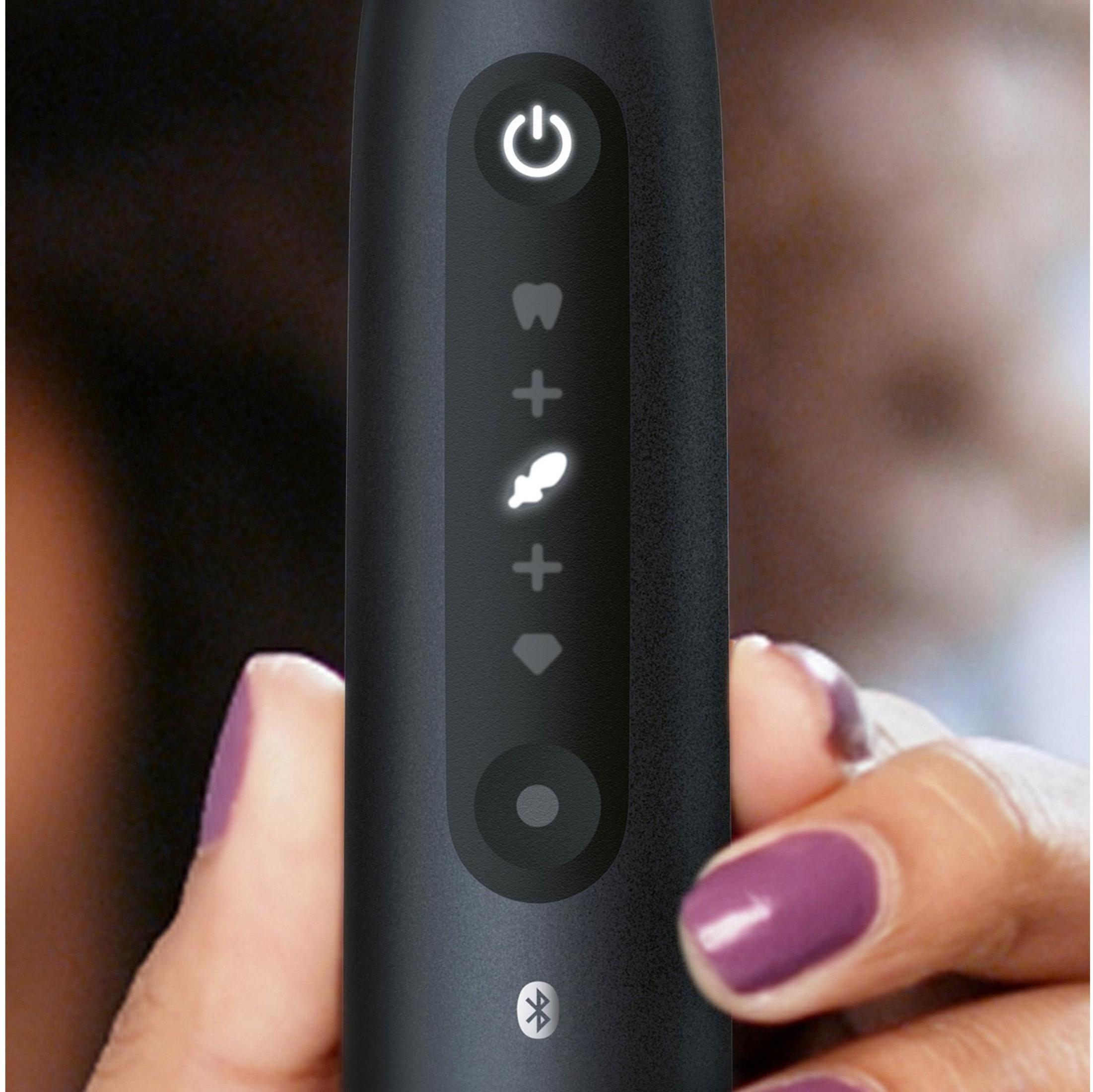 Dłoń trzyma czarną szczoteczkę do zębów z podświetlanymi ikonami: zasilanie, ząb, plus, błyskawica, plus, diament.