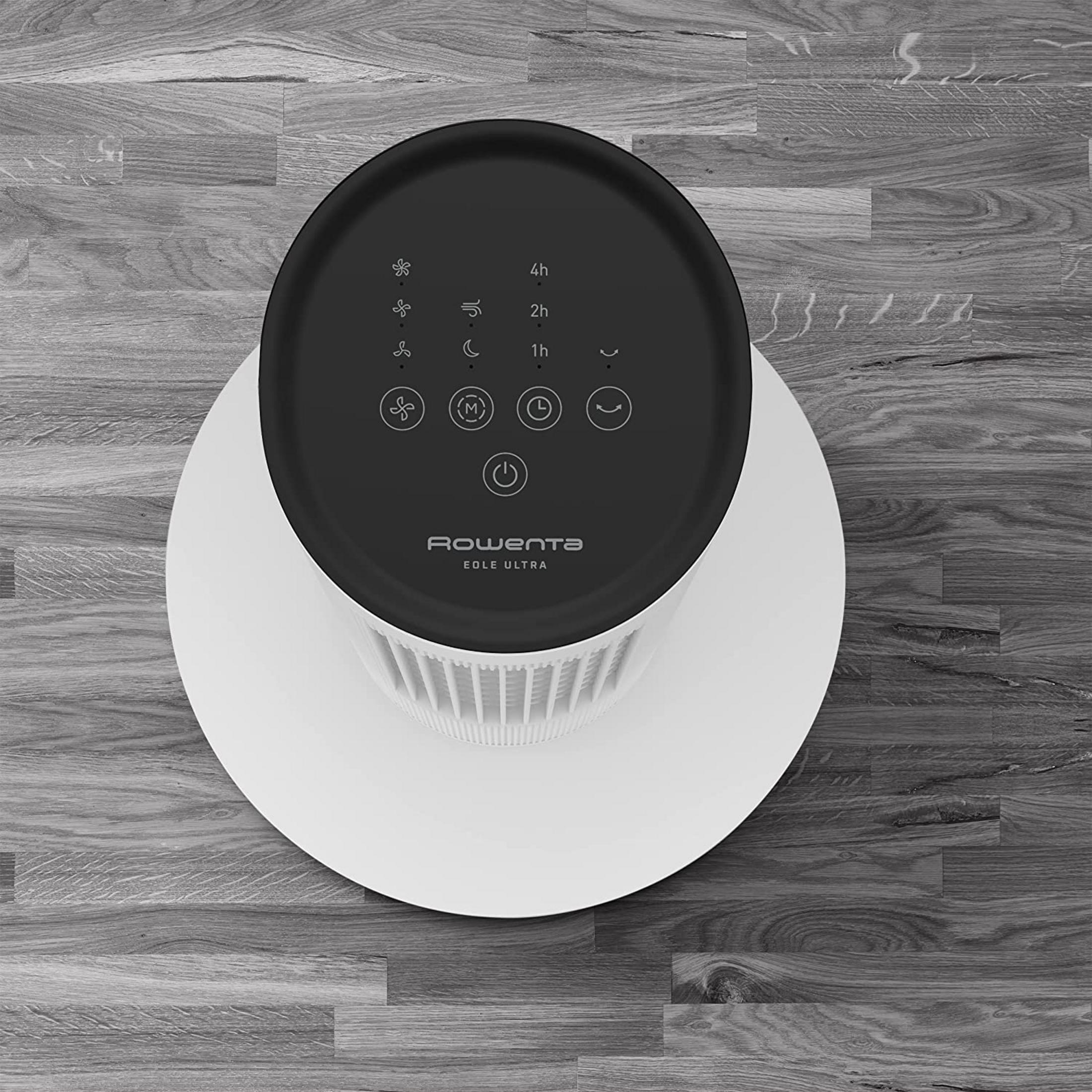 Biały wentylator z czarnym blatem i przyciskami na drewnianej podłodze.