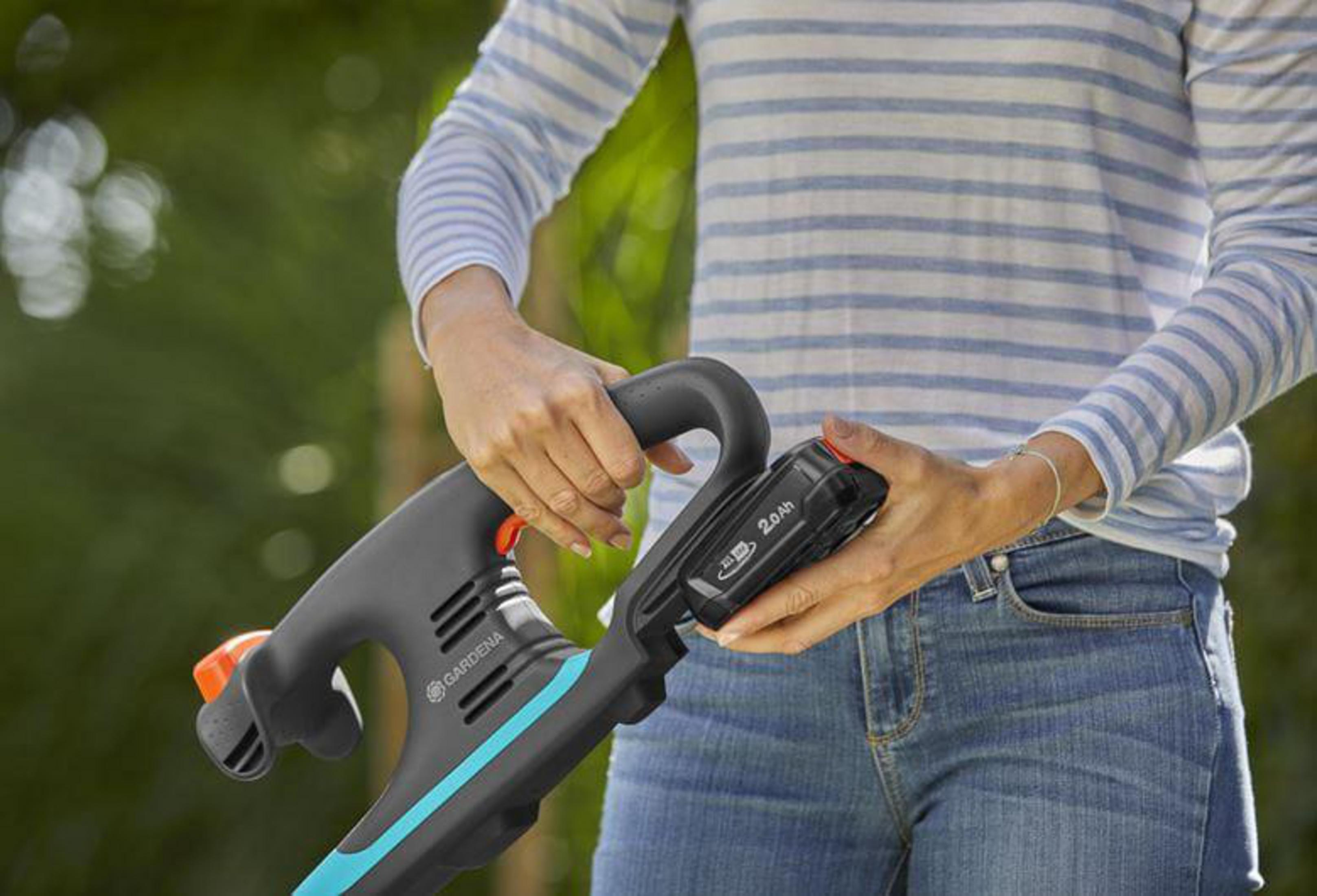 Osoba wkłada baterię do narzędzia ogrodniczego.