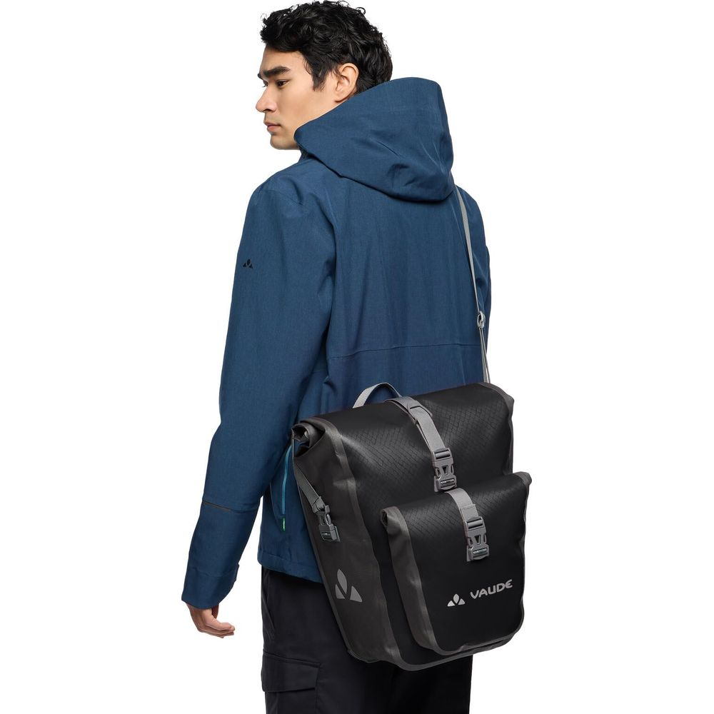 Mężczyzna w niebieskiej kurtce z torbą rowerową Vaude na ramieniu.