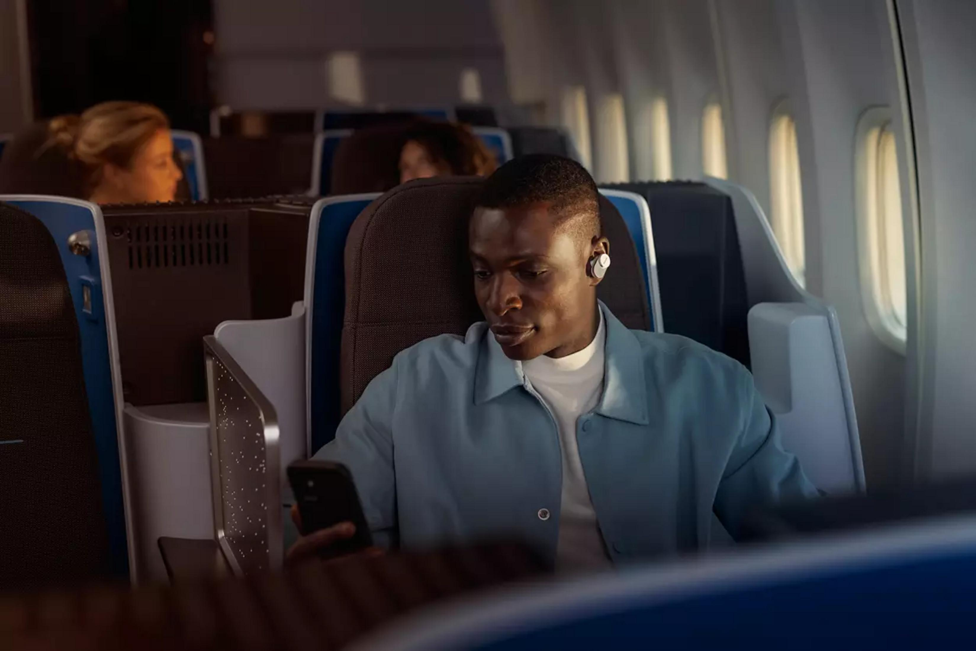 Mann mit Kopfhörern im Flugzeug, der auf sein Handy schaut.