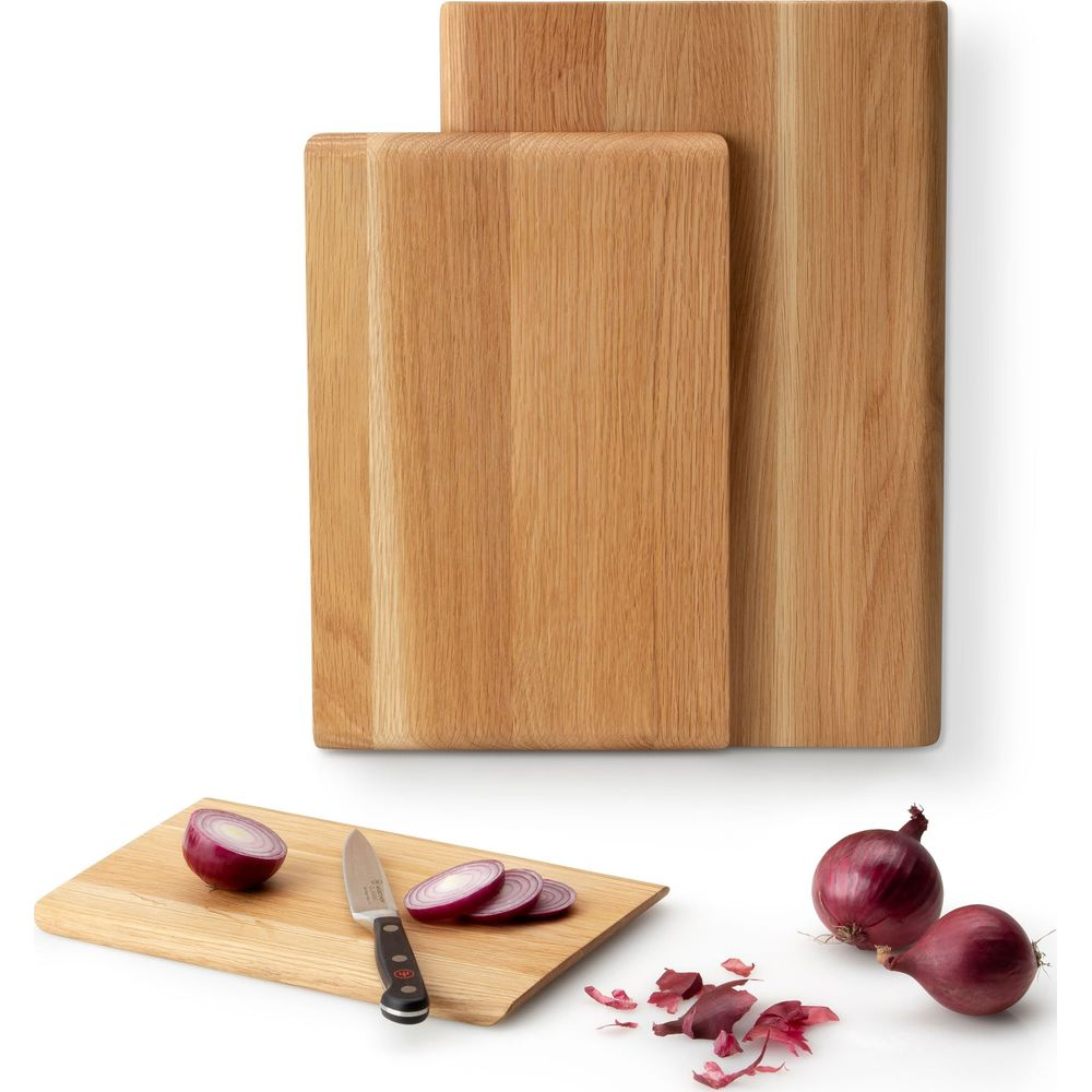 Zwei Holzschneidebretter, eines kleiner und vorne. Zwiebeln werden geschnitten.