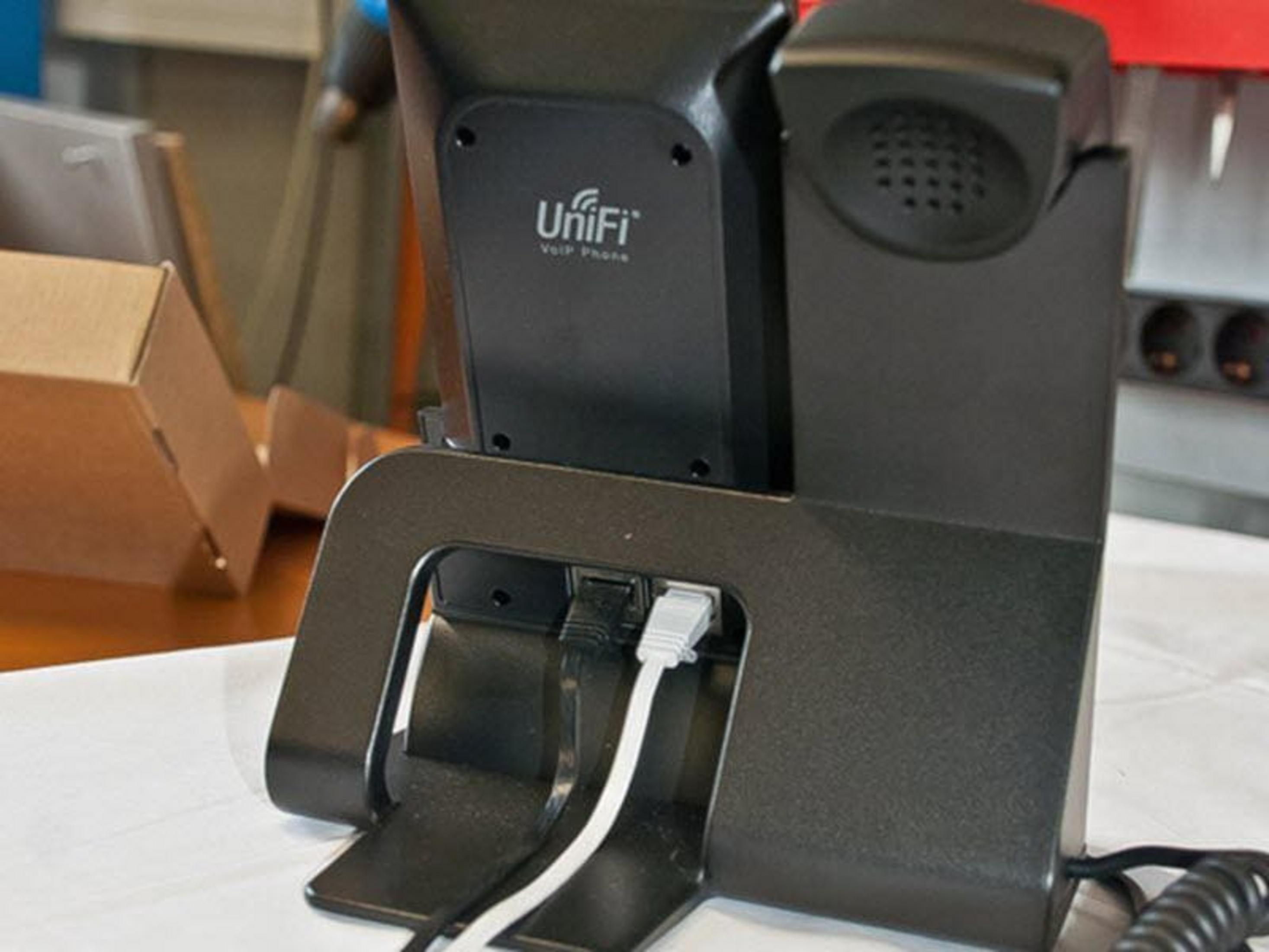 Un téléphone VoIP Unifi noir sur un support avec des câbles réseau branchés.