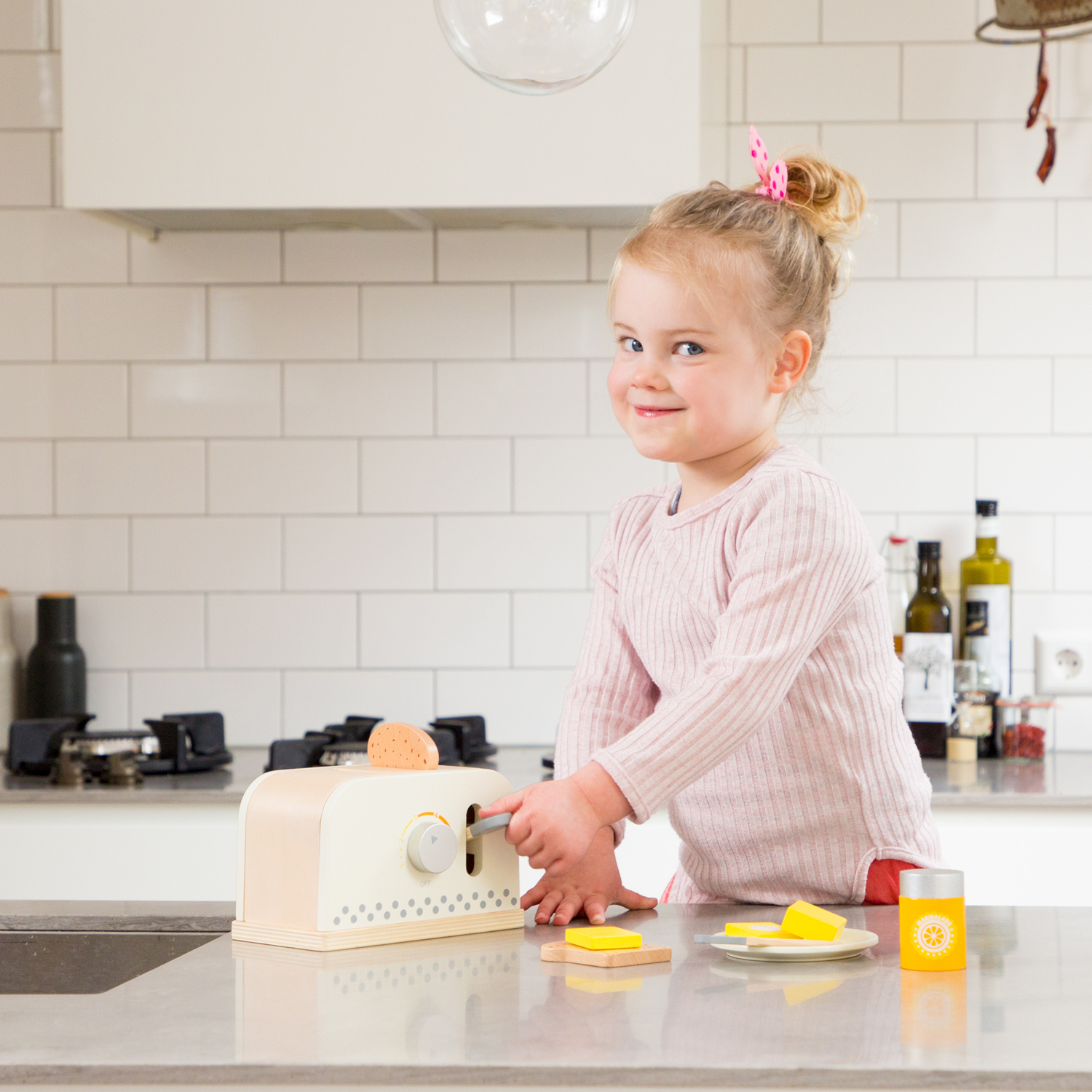 Una bambina gioca con un set da cucina giocattolo, tra cui tostapane, burro e succo.