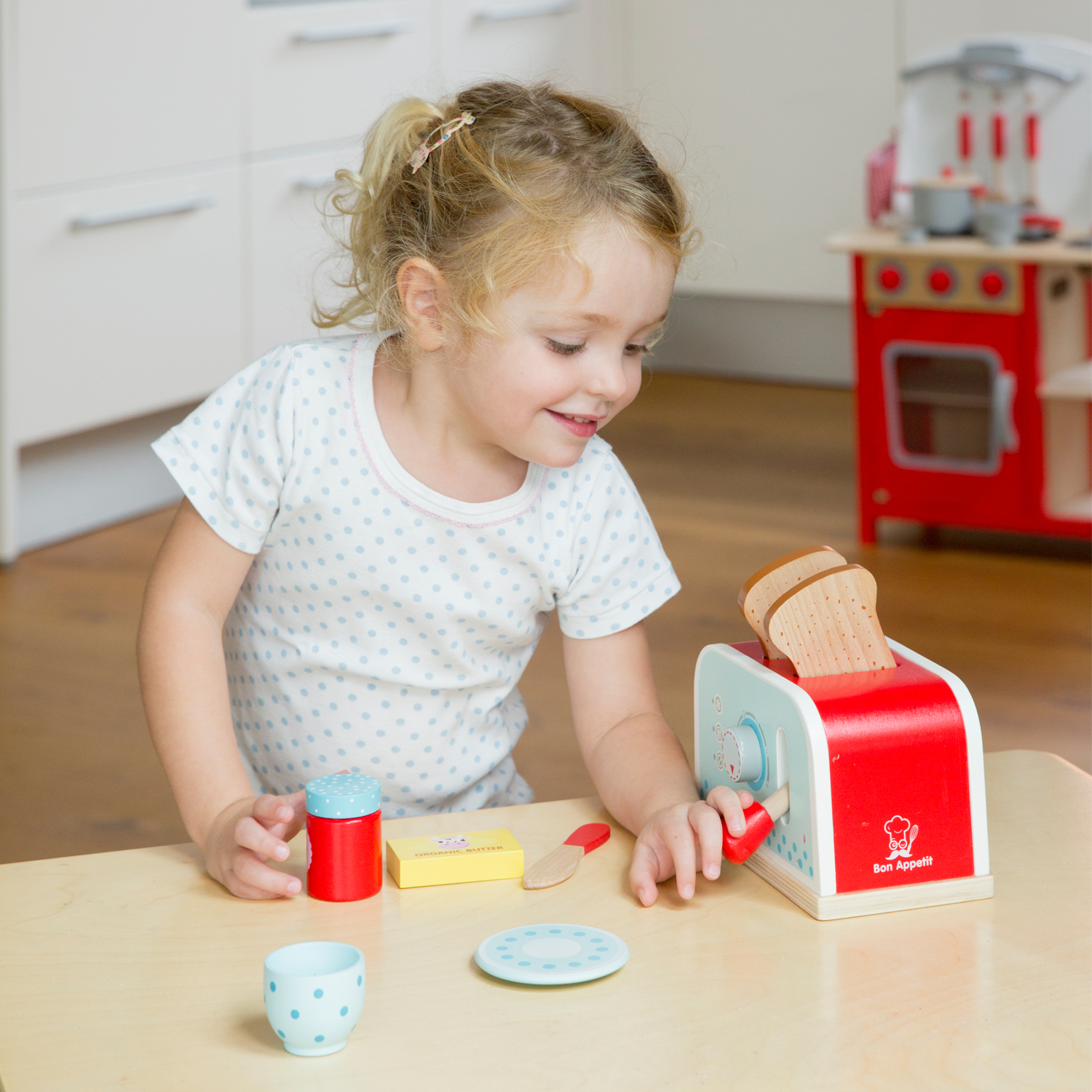 Una bambina gioca con un tostapane giocattolo, fette di pane e accessori.