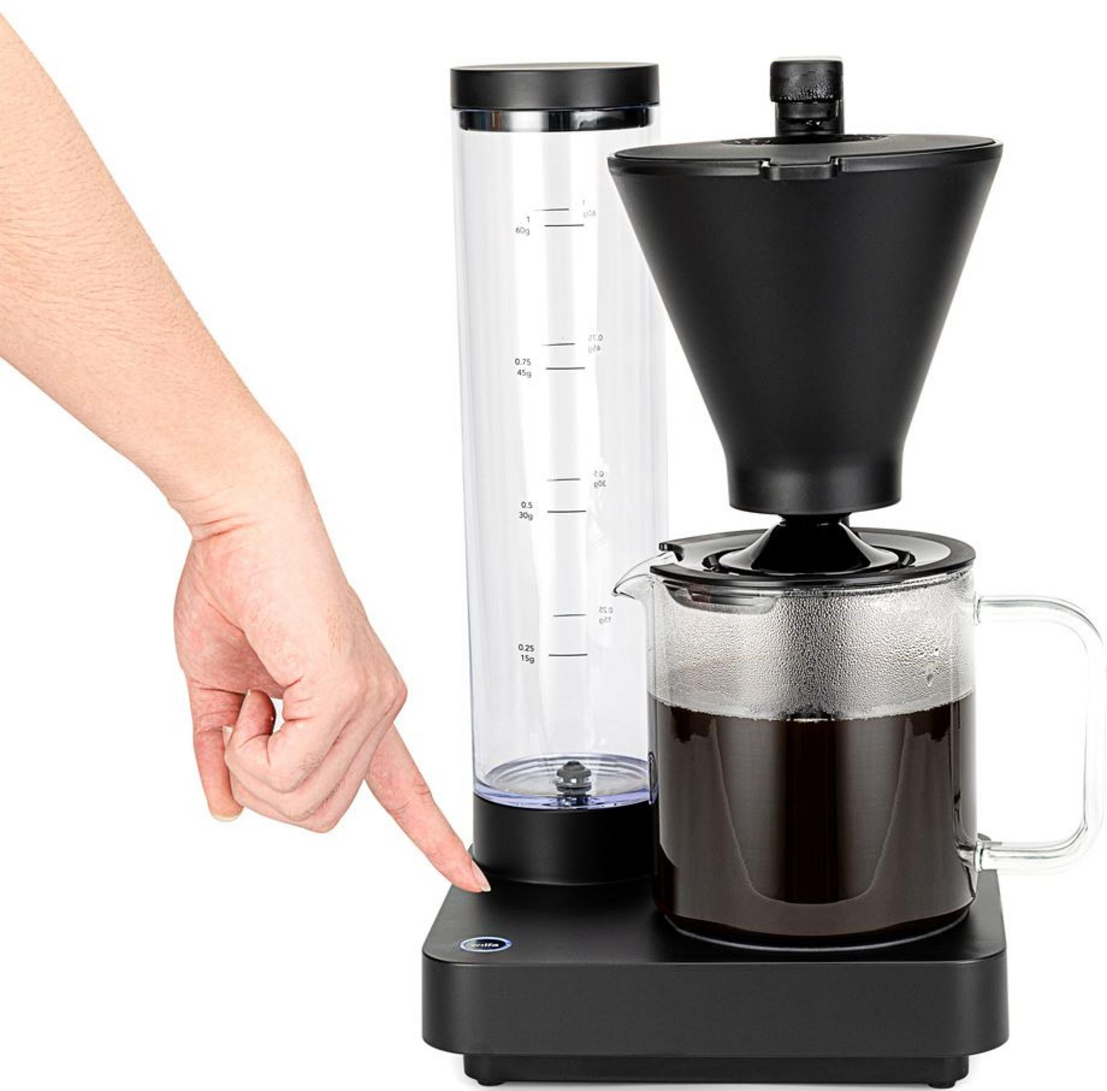 Una mano preme il pulsante di una caffettiera nera con caraffa in vetro.