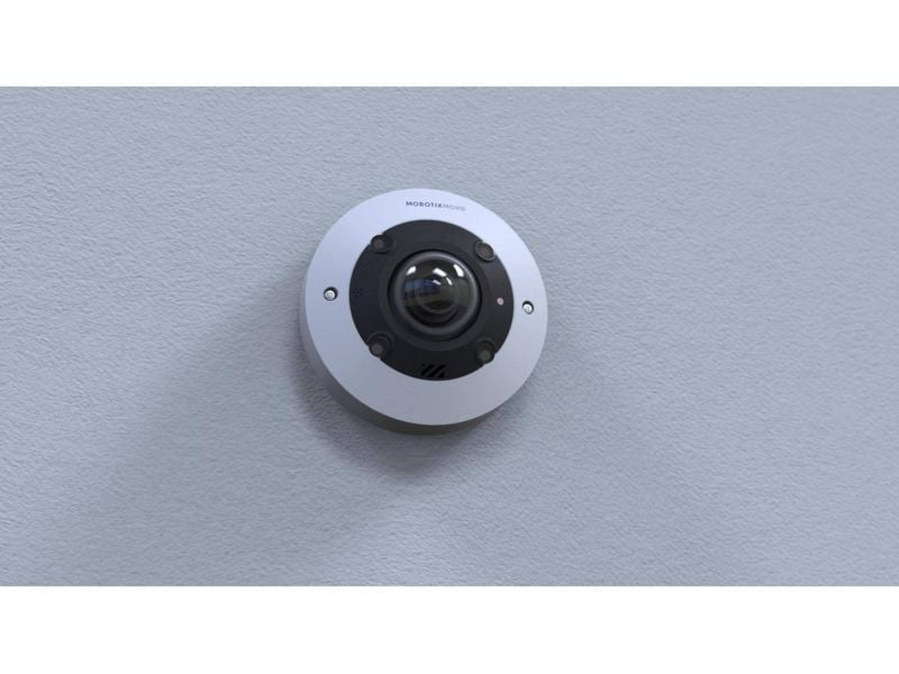 Biała kamera bezpieczeństwa z czarną soczewką zamontowana na szarej ścianie.