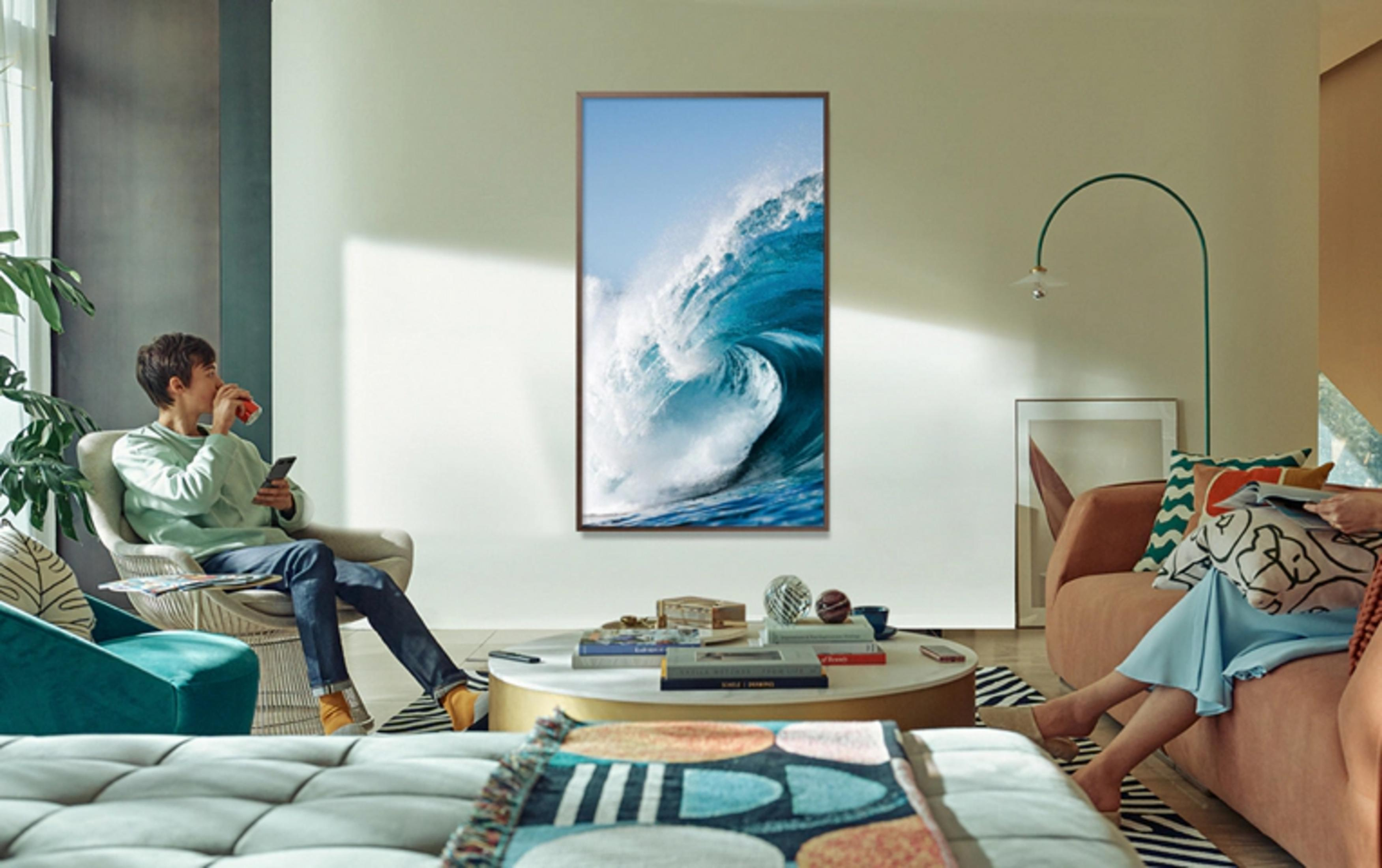 Homme assis dans fauteuil boit canette rouge, tient tel. Image vague accrochée au mur.