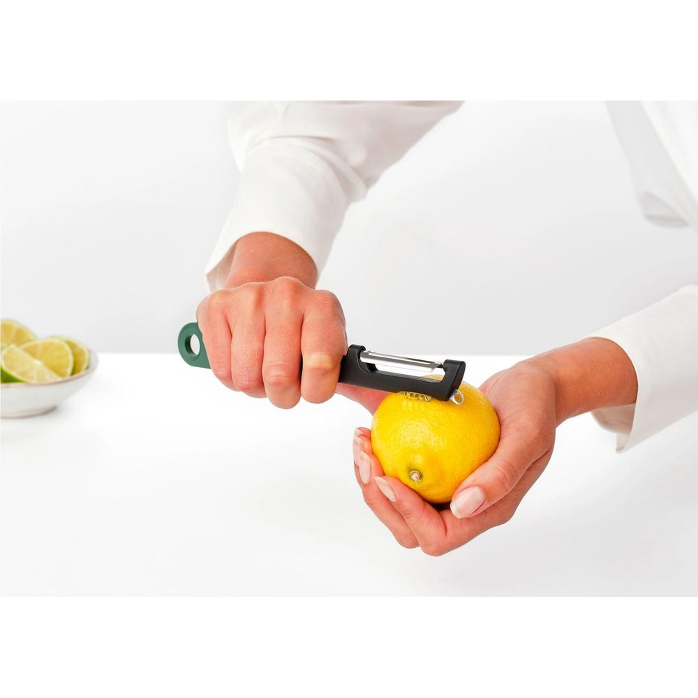 Hände schälen Zitrone mit schwarzem Sparschäler. Schüssel mit Limettenscheiben.