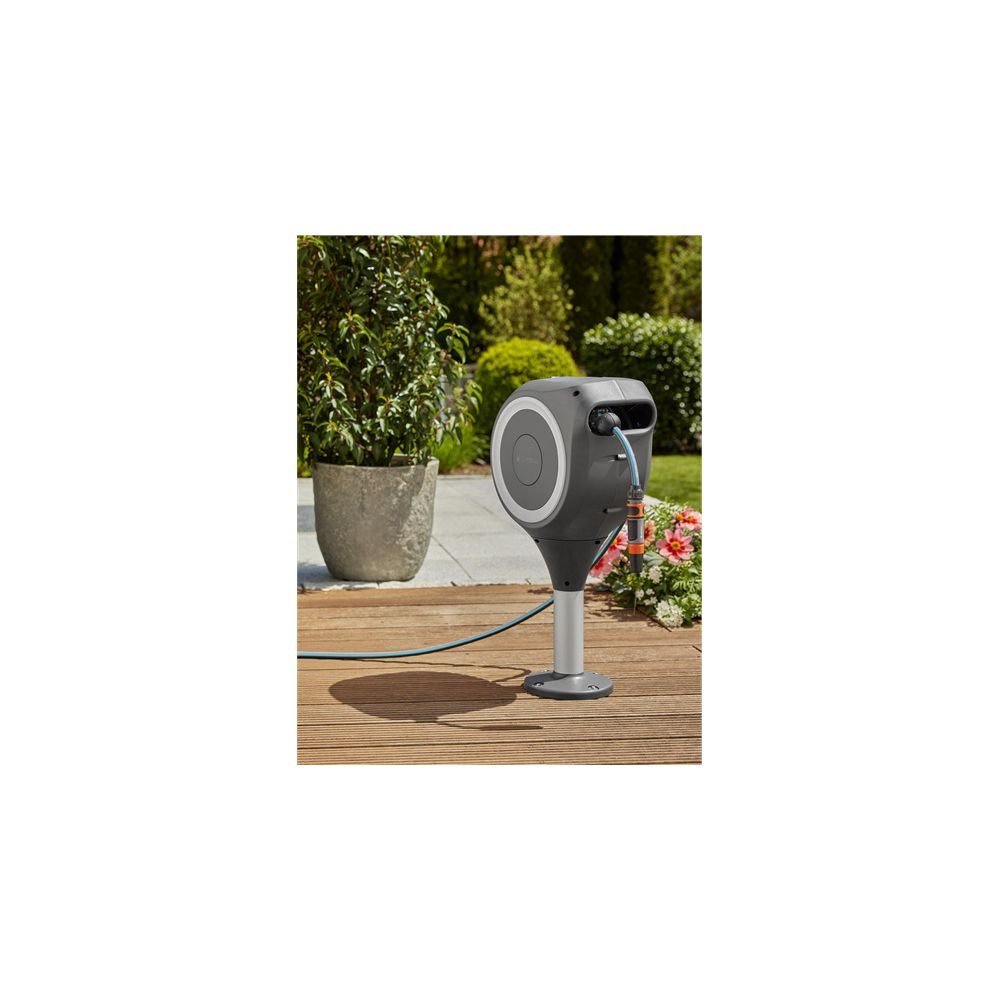 Ein dunkler Gartenschlauchhalter mit Schlauch auf Holzdeck, neben Topfpflanze und Blumen.