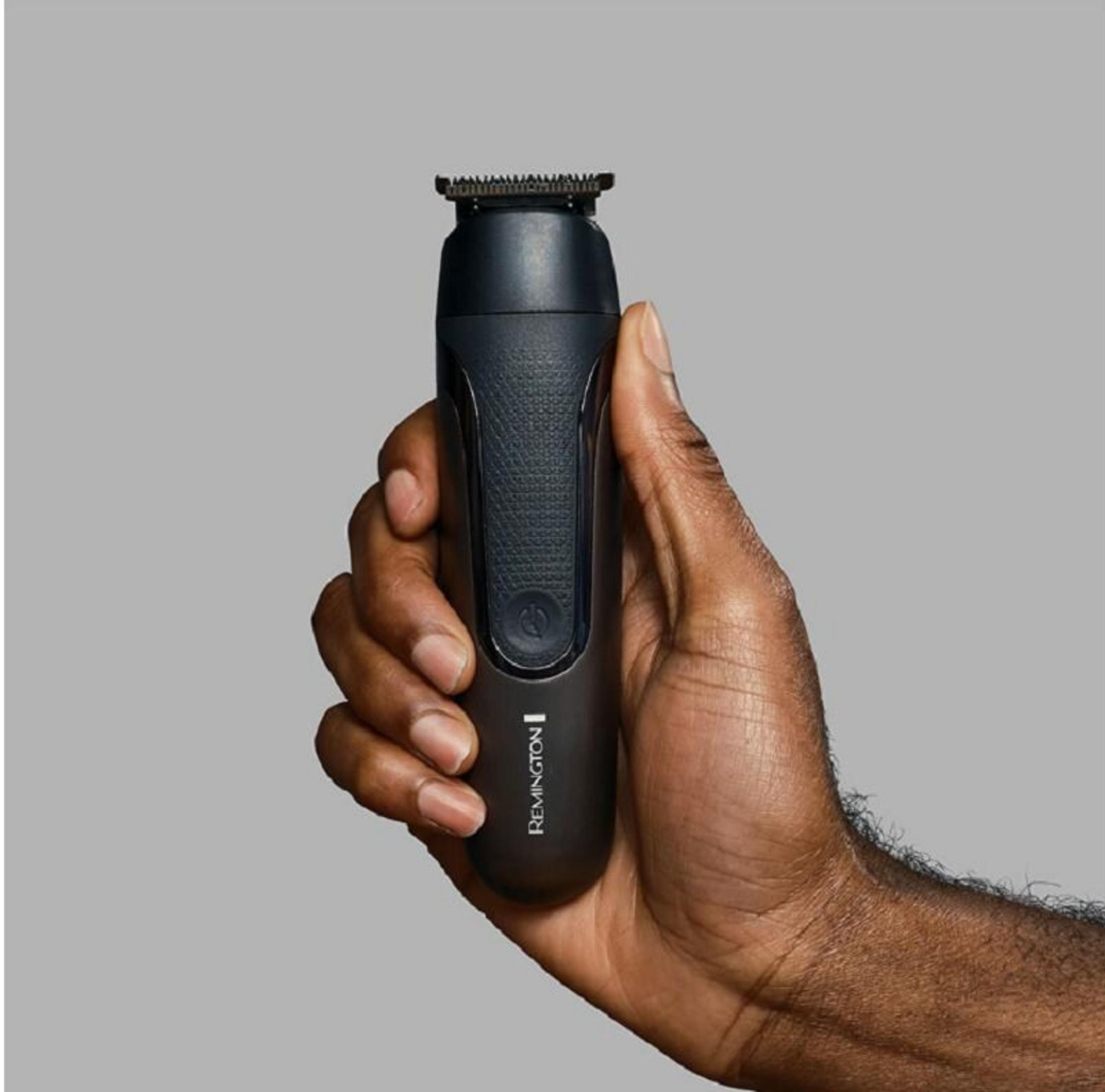 Eine Hand hält einen schwarzen Remington Trimmer vor grauem Hintergrund.