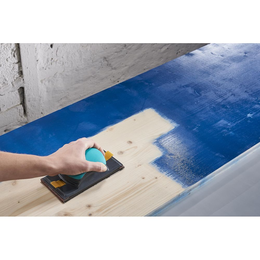 Une main utilise un bloc de ponçage pour travailler sur une surface bleue.