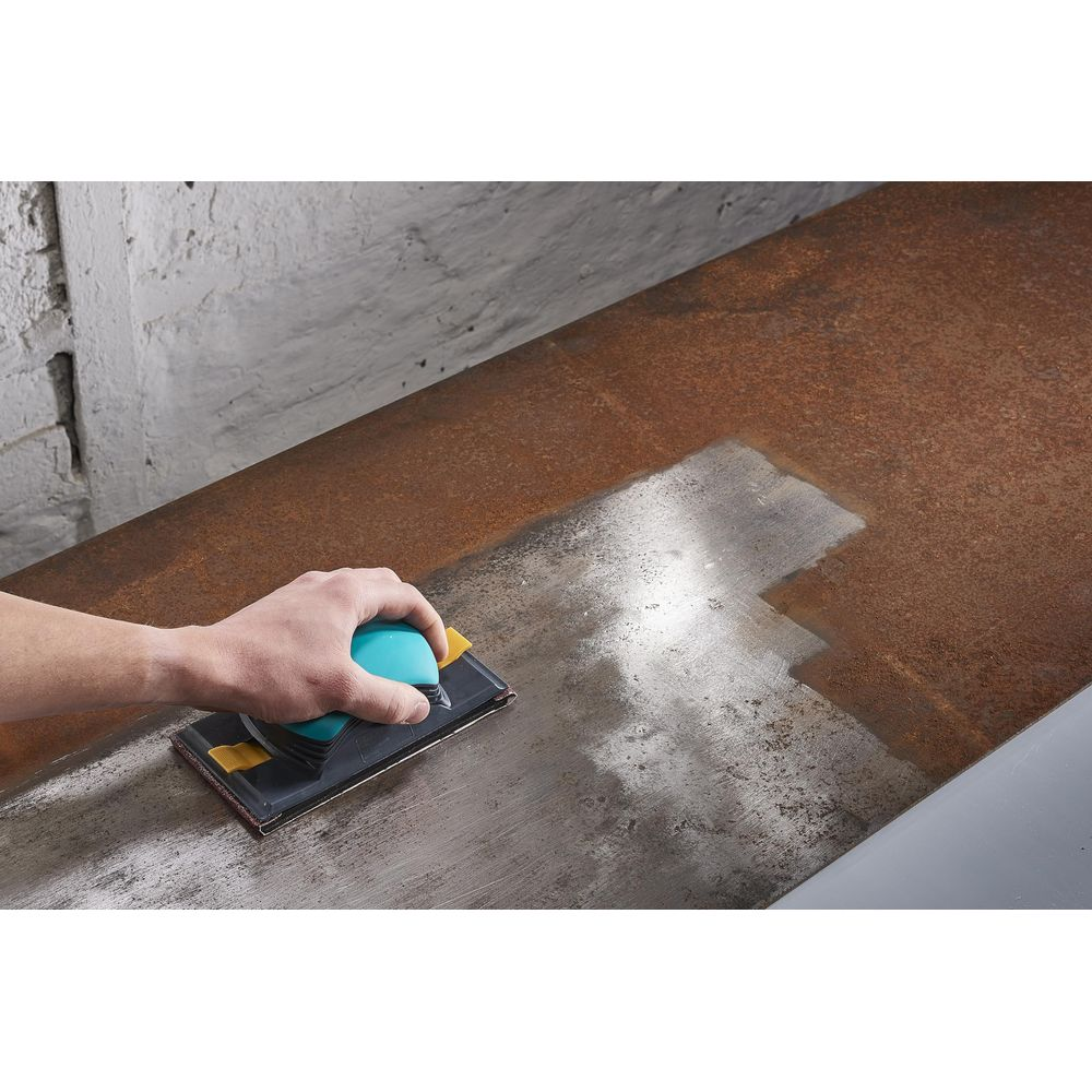 Main ponçant du métal rouillé avec bloc bleu, révélant une surface propre.