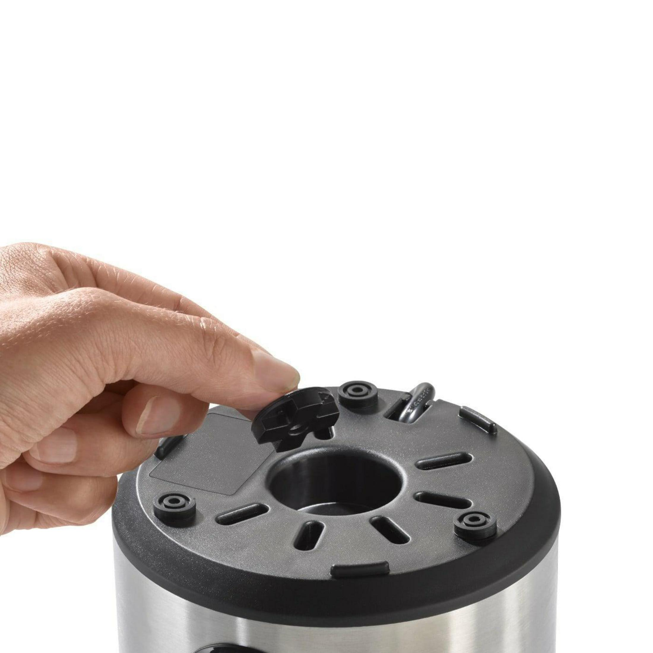 Une main appuie sur un capuchon noir en plastique sur un appareil métallique.