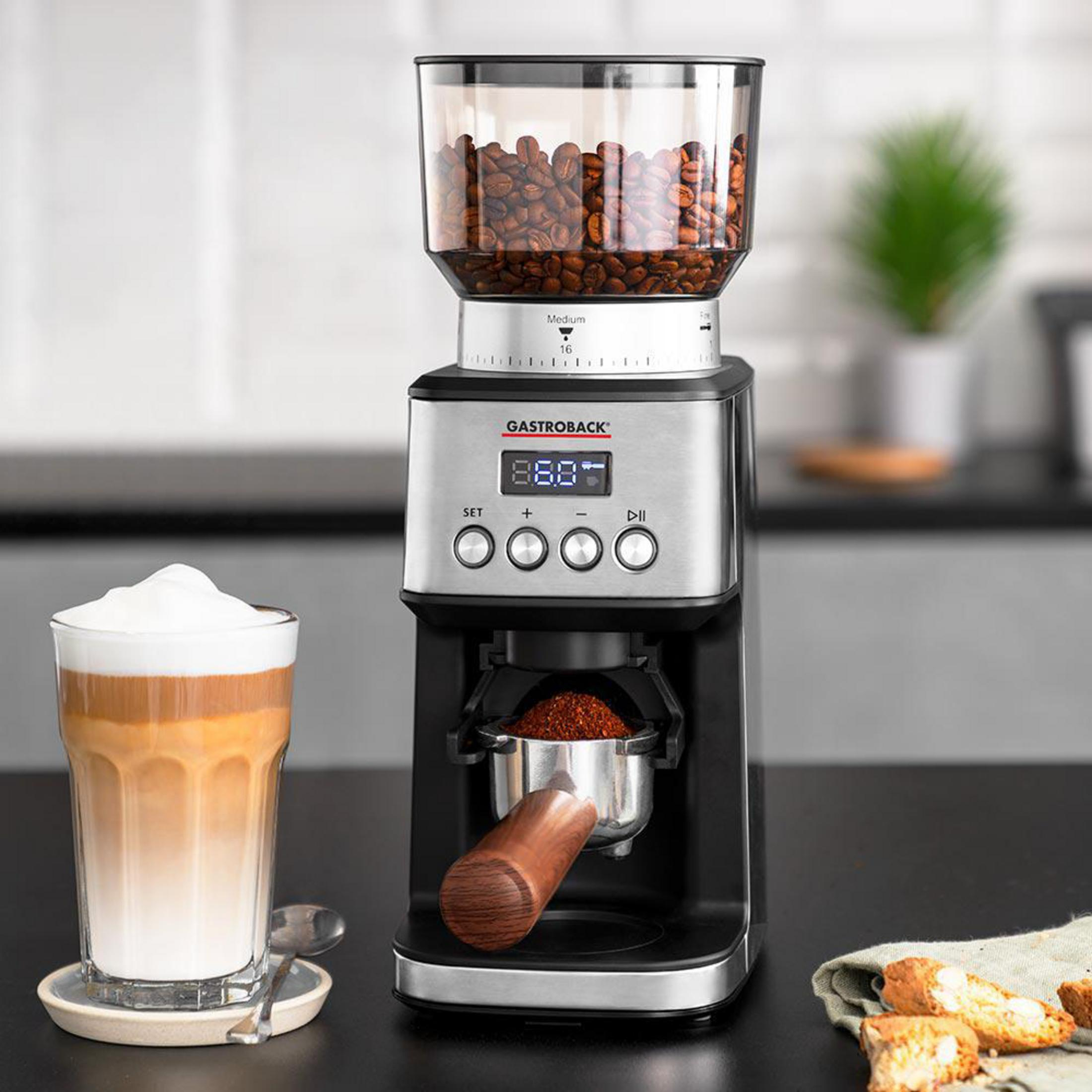 Kaffeemühle mit Glasbehälter voller Bohnen, daneben ein Latte Macchiato.