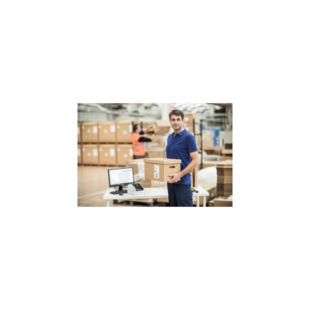 Mężczyzna w magazynie trzymający pudełko przed komputerem i regałami.