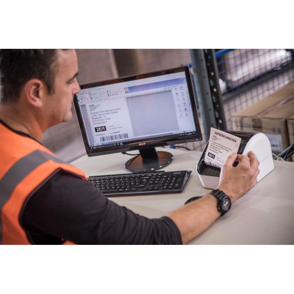 Mężczyzna w kamizelce ostrzegawczej siedzi przy komputerze, obsługuje drukarkę etykiet.