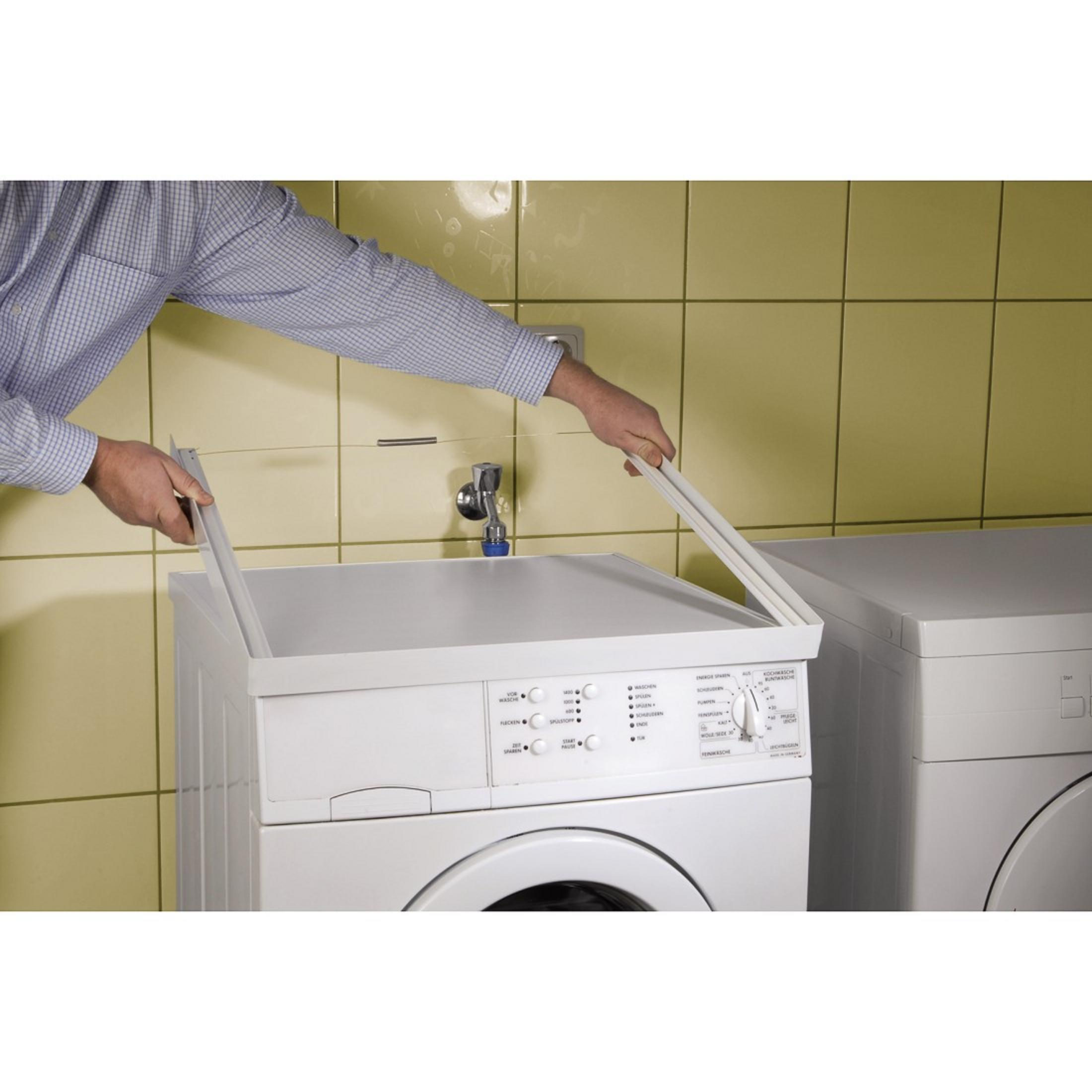 Mann montiert weiße Waschmaschine mit weißem Rahmen. Gelbe Fliesen im Hintergrund.