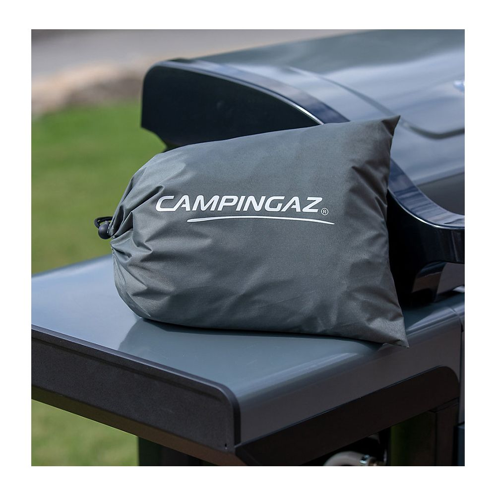 Funda gris Campingaz sobre una mesa de barbacoa exterior.