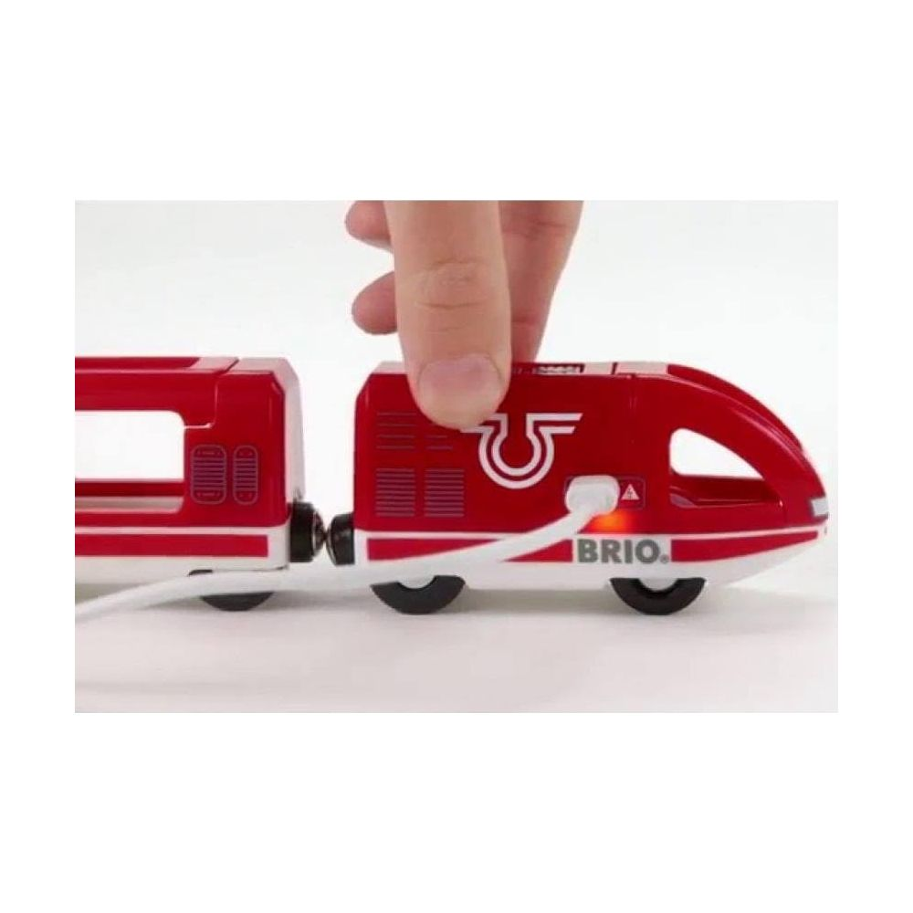 Czerwony pociąg BRIO podłączony białym kablem. Ręka trzyma lokomotywę.