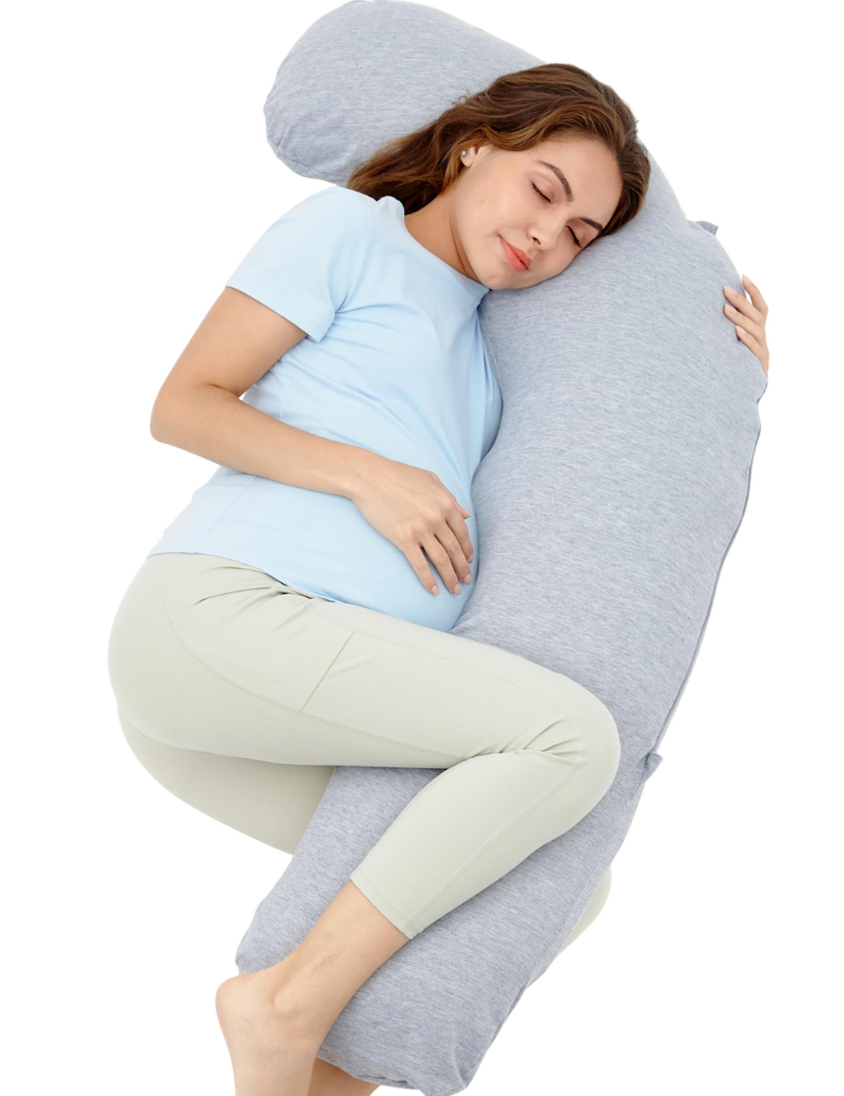 Donna incinta dorme su cuscino grigio, indossa top azzurro e pantaloni beige.